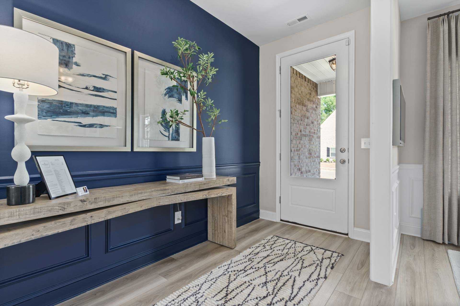 Stylish entryway in Creek Grove home, New Market AL with navy accent wall, abstract art, potted plant, wooden console, and front door