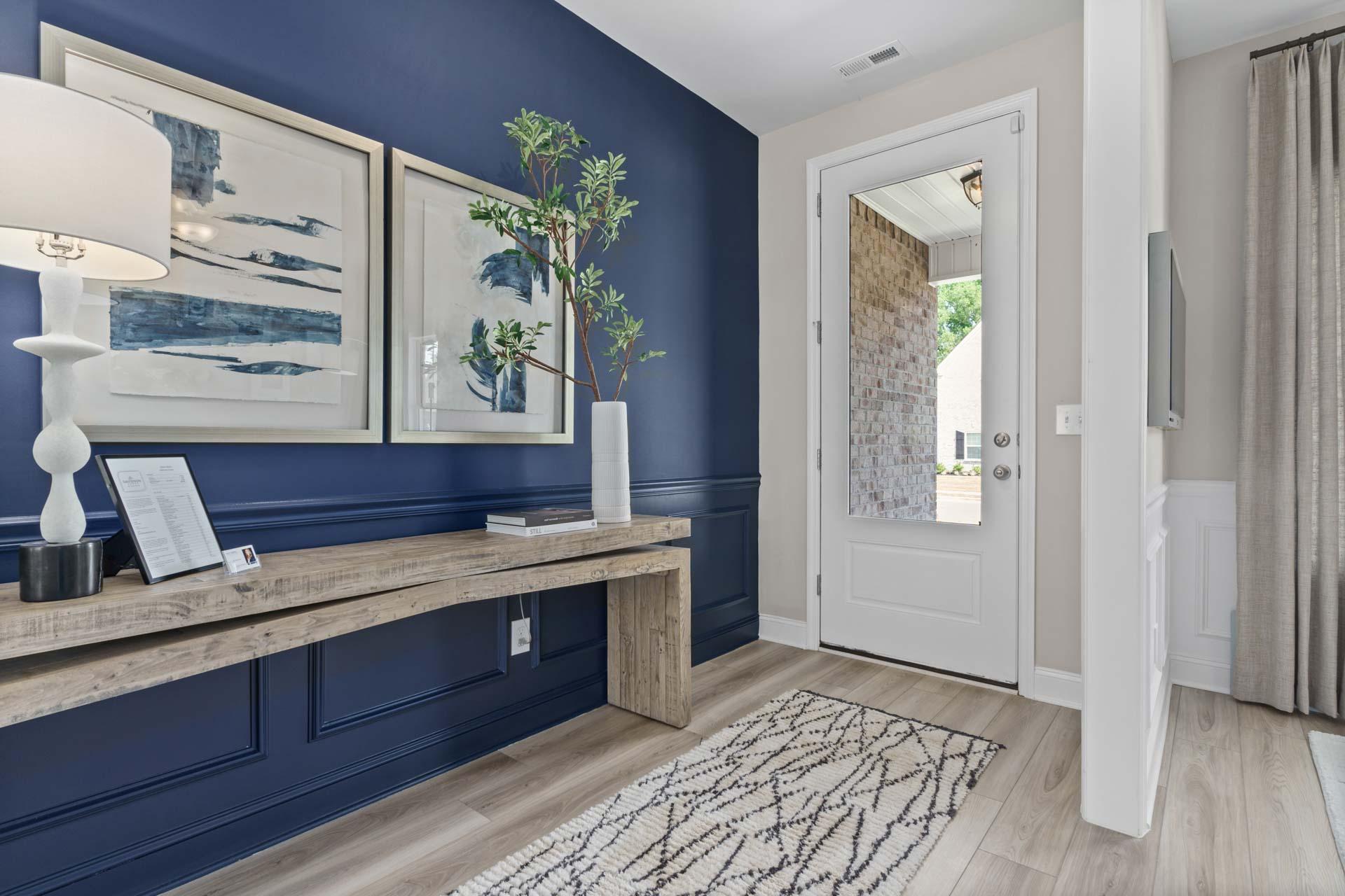 Stylish entryway in Creek Grove home, New Market AL with navy accent wall, abstract art, potted plant, wooden console, and front door