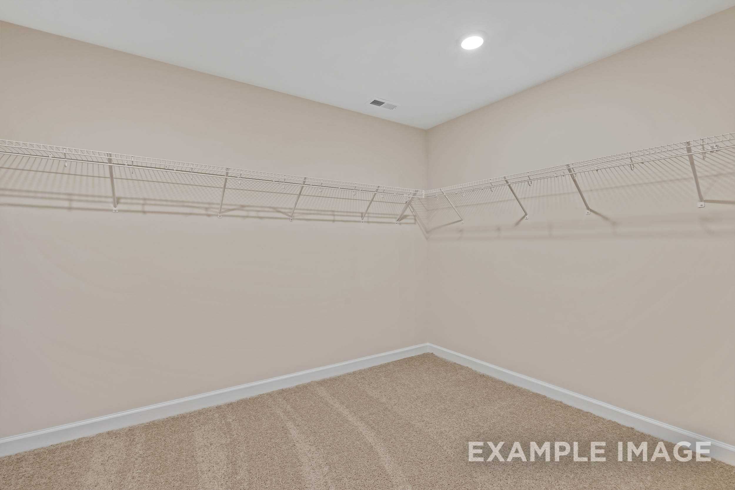 Spacious walk-in closet in The Preston A master suite featuring wire shelving, hanging rods, and beige walls with carpeted floor