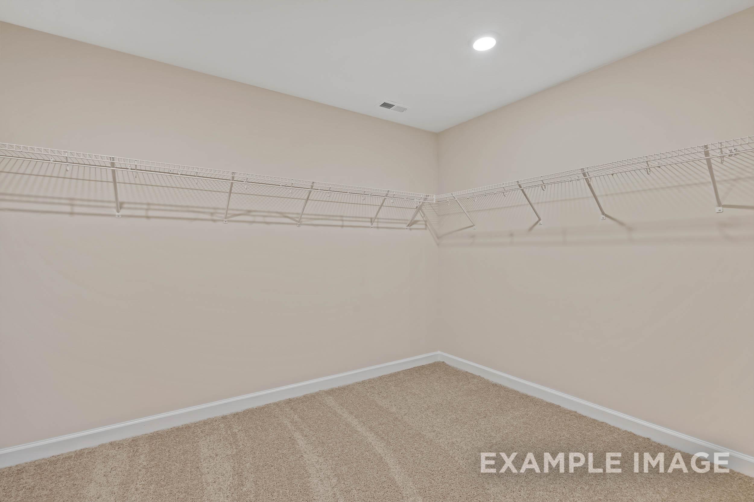 Spacious walk-in closet in The Preston A master suite featuring wire shelving, hanging rods, and beige walls with carpeted floor