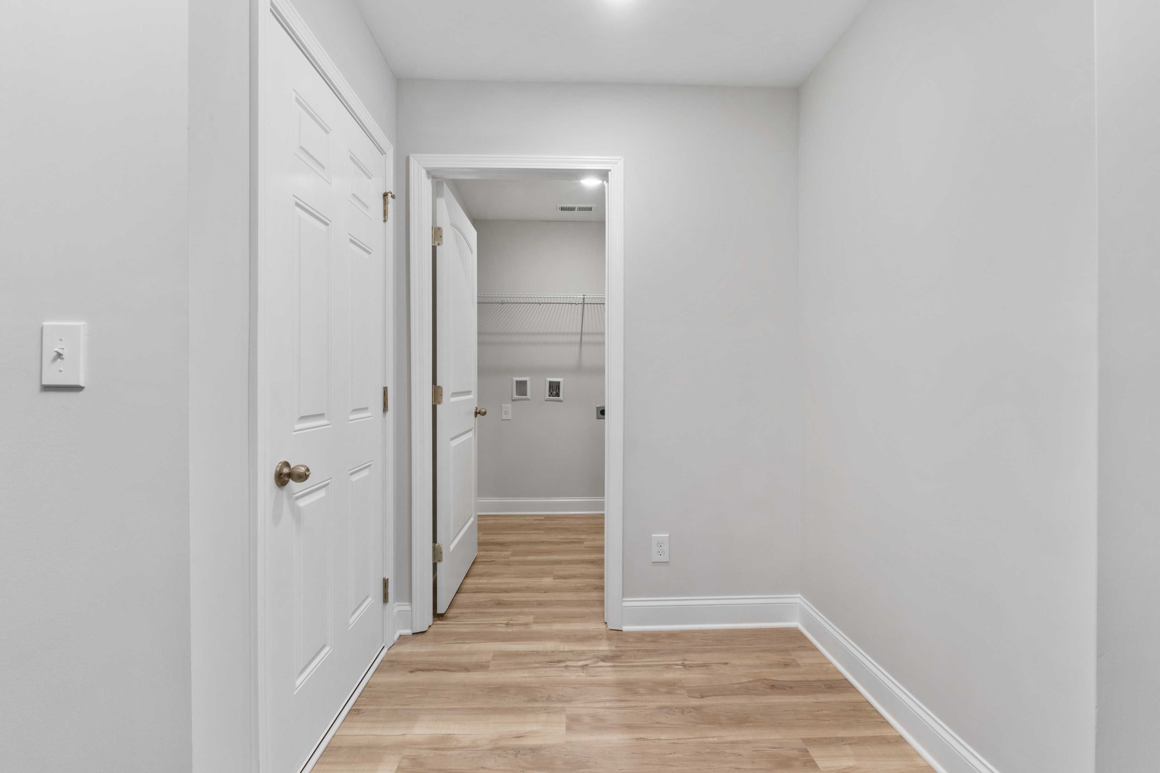 Laundry room interior at Collins Lane in Meridianville AL with gray walls, white doors, open shelves, and light wood floors by Davidson Homes