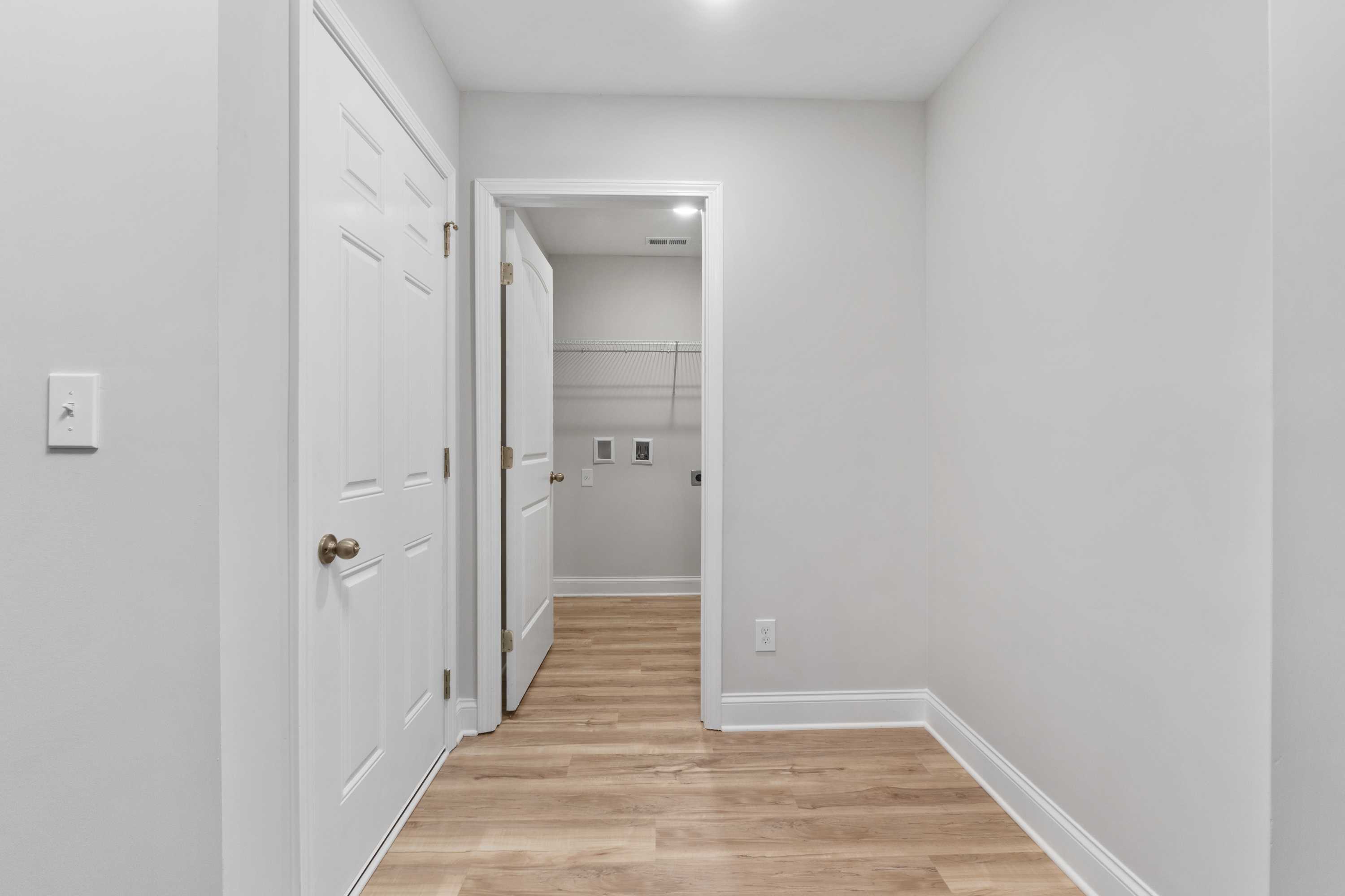 Laundry room interior at Collins Lane in Meridianville AL with gray walls, white doors, open shelves, and light wood floors by Davidson Homes