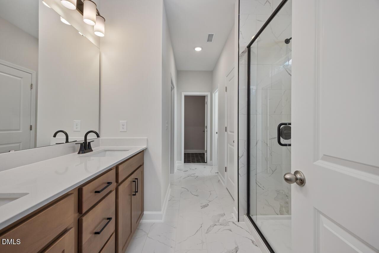 Primary bathroom with wood vanity, marble-style tile, and glass shower in The Ashport L at Sage on North Main, Wake Forest.