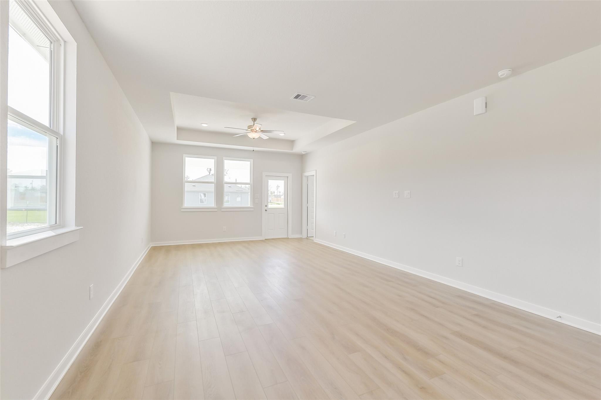 Spacious living room with light oak floors, tray ceiling, ceiling fan, and large windows in Davidson Homes The Frio G, Conroe, Texas