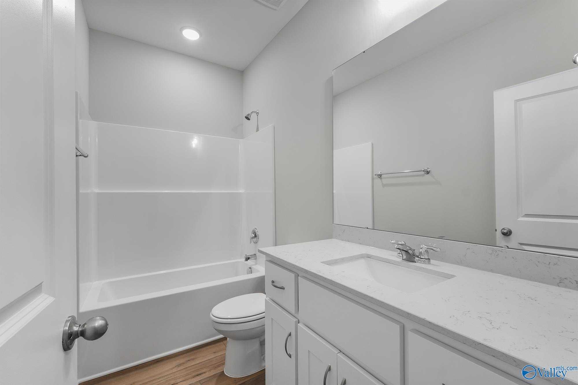 Modern secondary bathroom featuring white bathtub-shower combo, vanity, and mirror in The Daphne D by Davidson Homes, Athens, AL