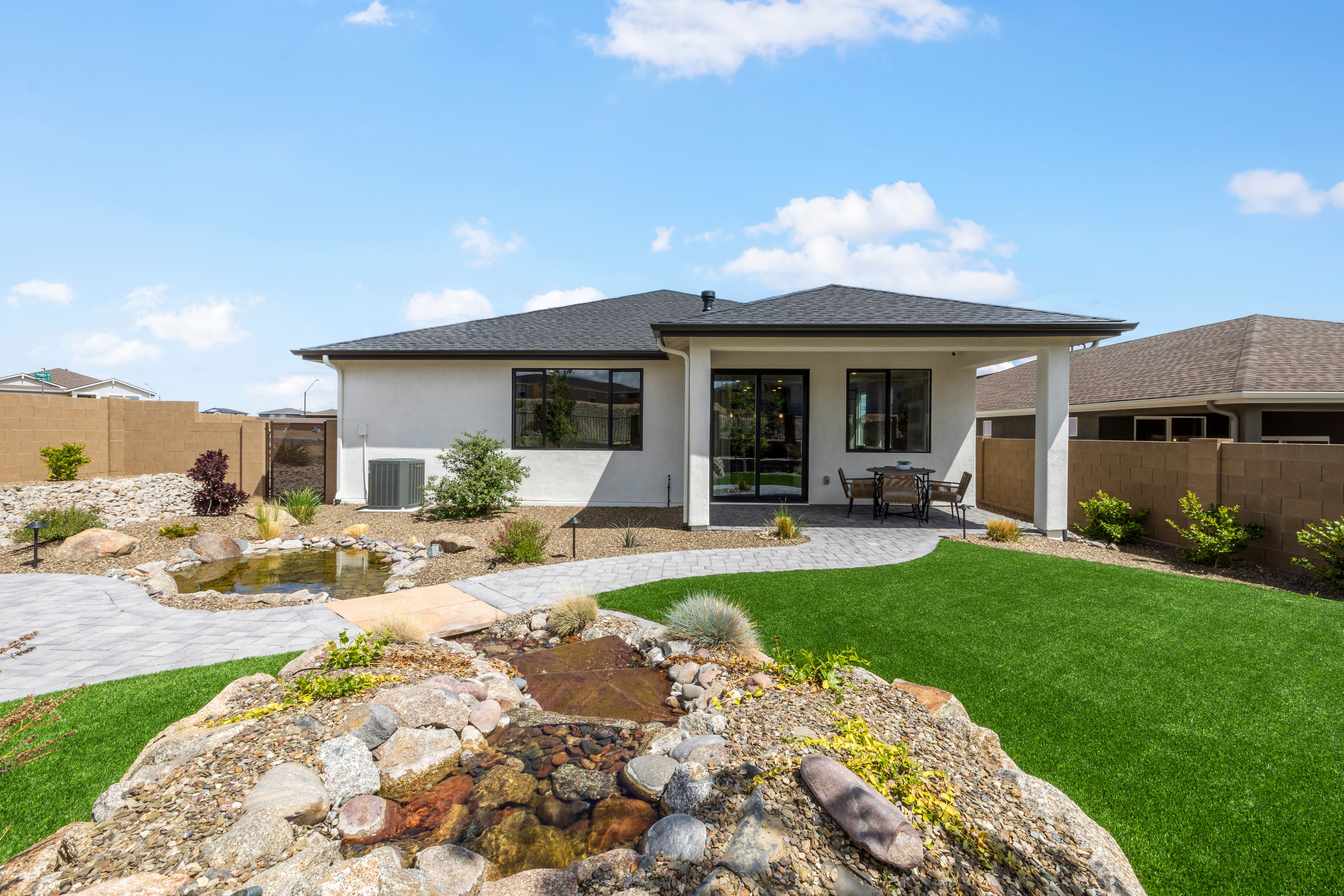 Contemporary backyard at South Ranch Western Collection in Prescott AZ featuring covered patio, large glass doors, rock pond water feature, paver paths, and turf lawn