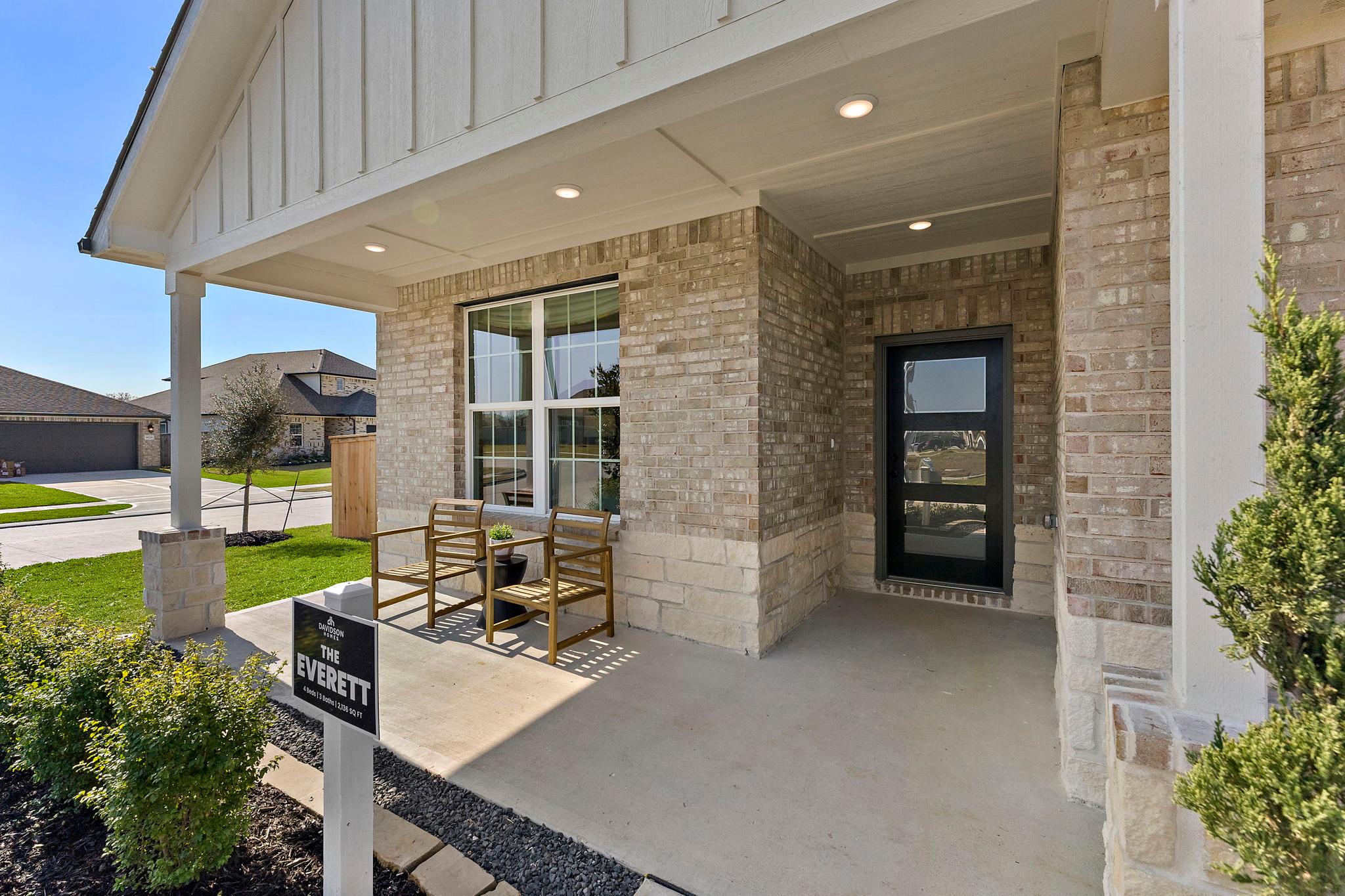 Everett model brick home with covered front porch, large windows, and patio seating at Sundance Cove in Crosby, Texas