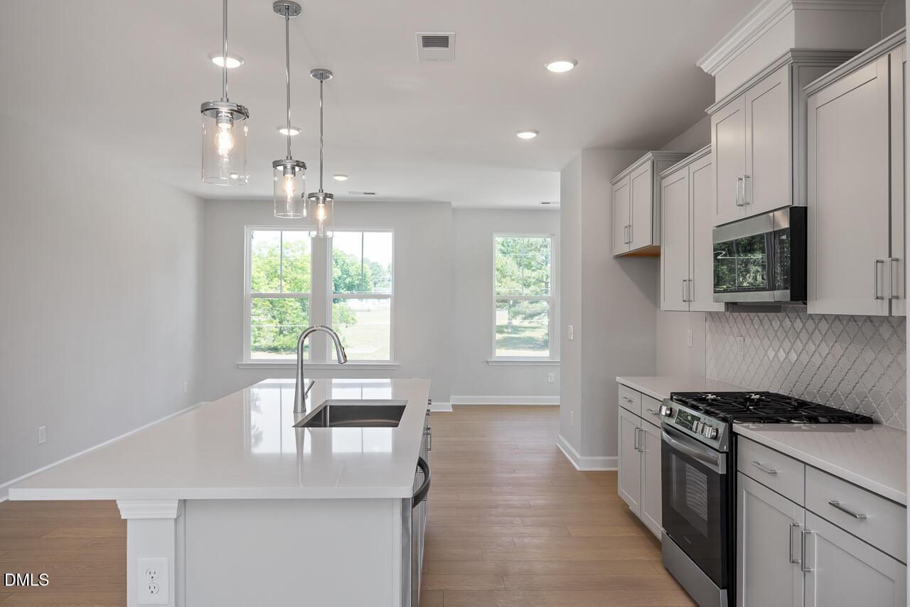 Modern kitchen with quartz island, gray cabinets, and stainless appliances in The Mitchell floor plan, Camden Park, NC.
