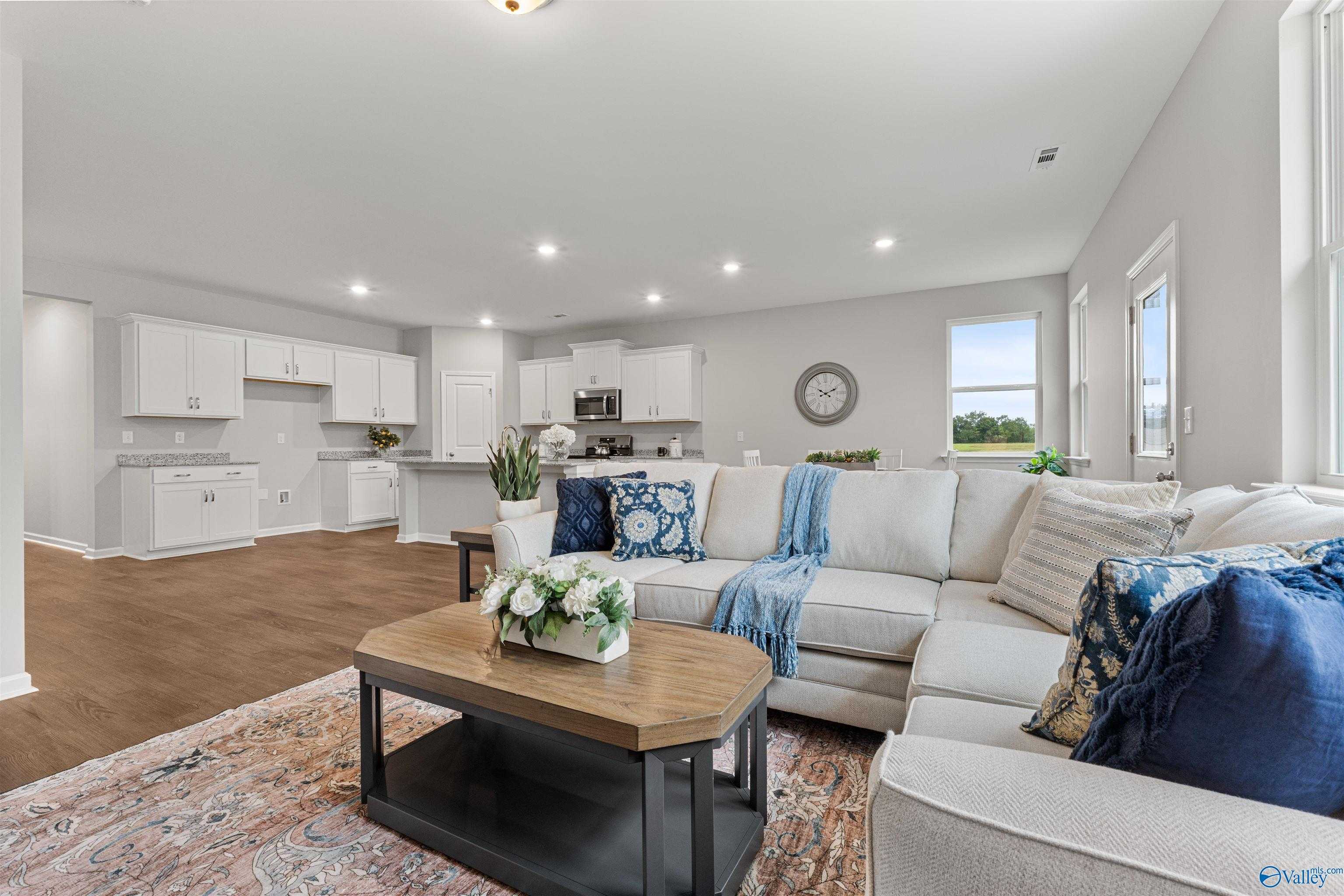 Spacious living room with white L-shaped sectional, hardwood floors, and open kitchen in Davidson Homes The Phoenix, Fayetteville, TN