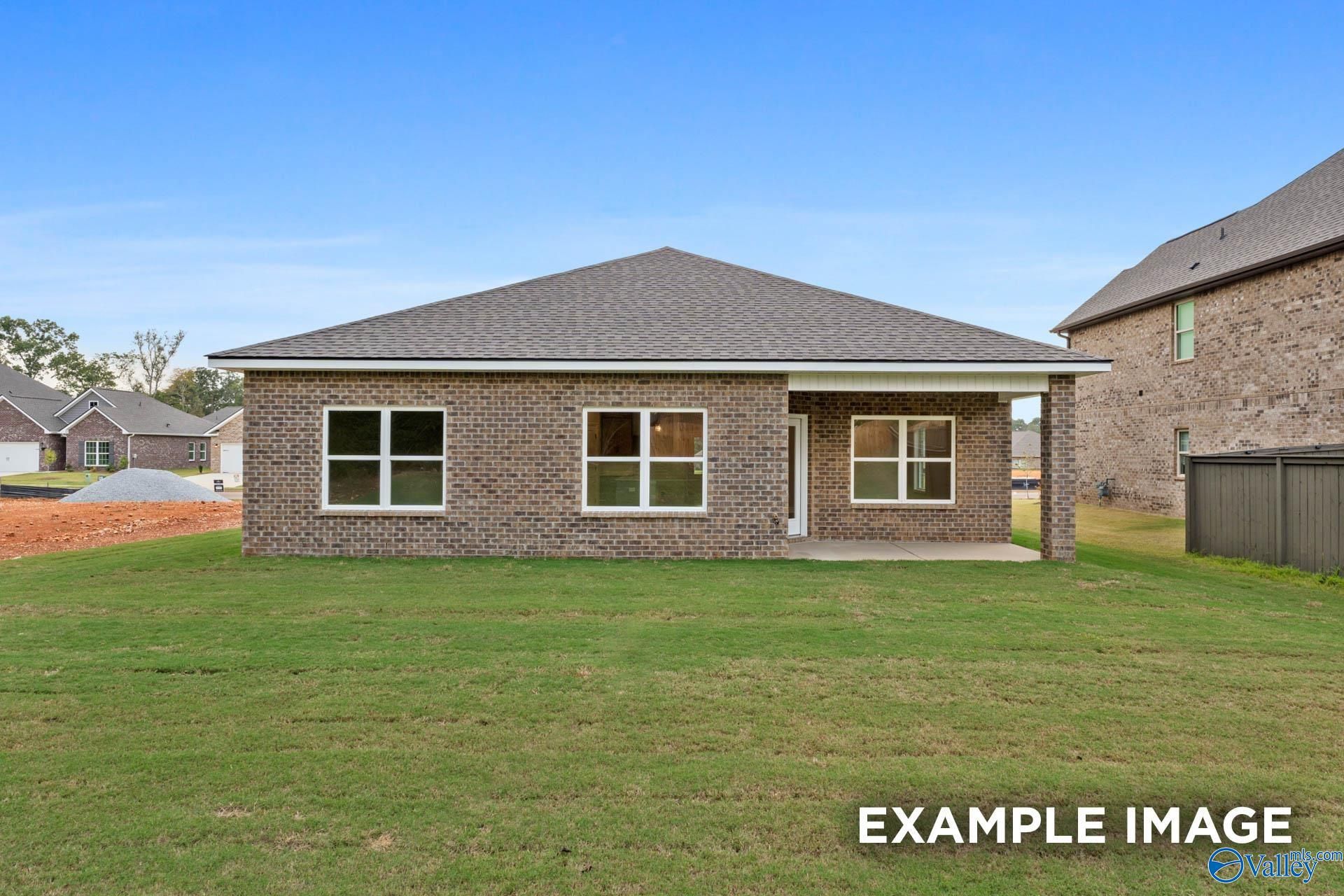 Rear view of brick 3-bedroom home with covered patio, lush green backyard in Wood Trail, Toney, Alabama by Davidson Homes