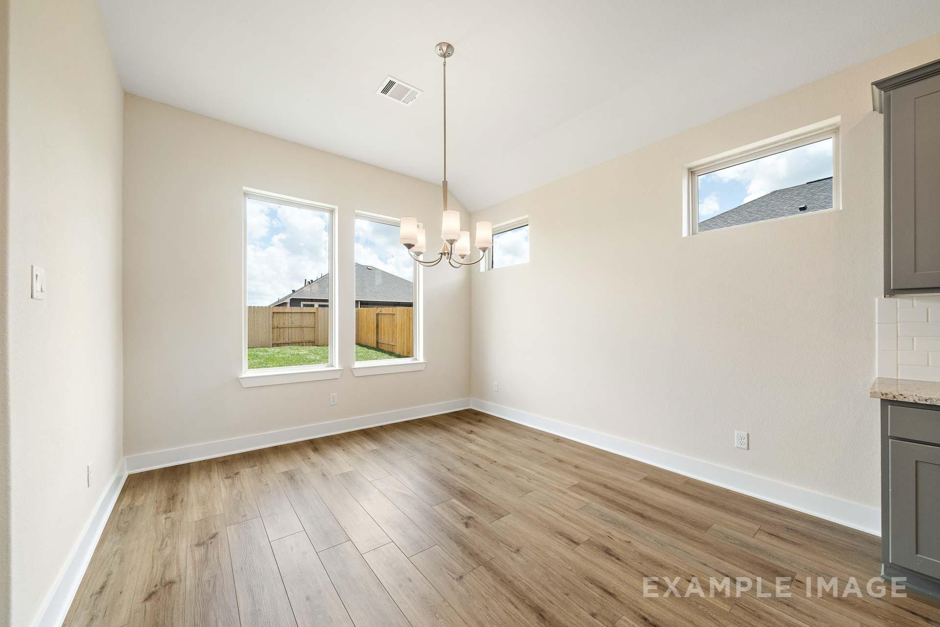 Spacious dining room in The Diana C with pendant chandelier, large windows overlooking backyard, hardwood floors, adjacent gray cabinet kitchen