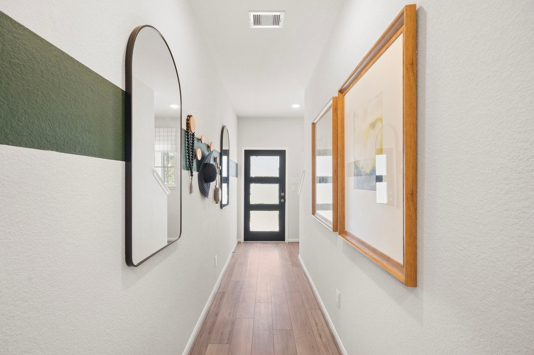 Spacious hallway at Caney Creek Place in Conroe Texas with hardwood floors, arched mirror, wall art, hats and black front door
