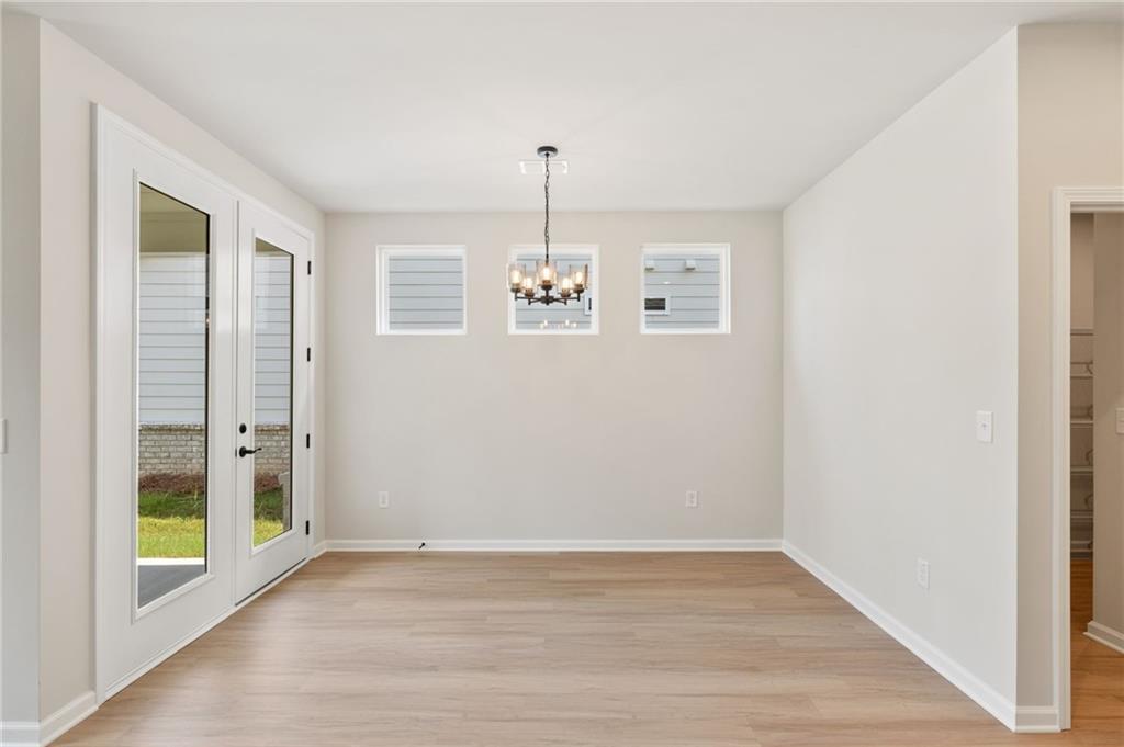 Bright dining room with French doors to lush backyard, hardwood floors, chandelier, and windows in The Laurel J, Loganville, GA