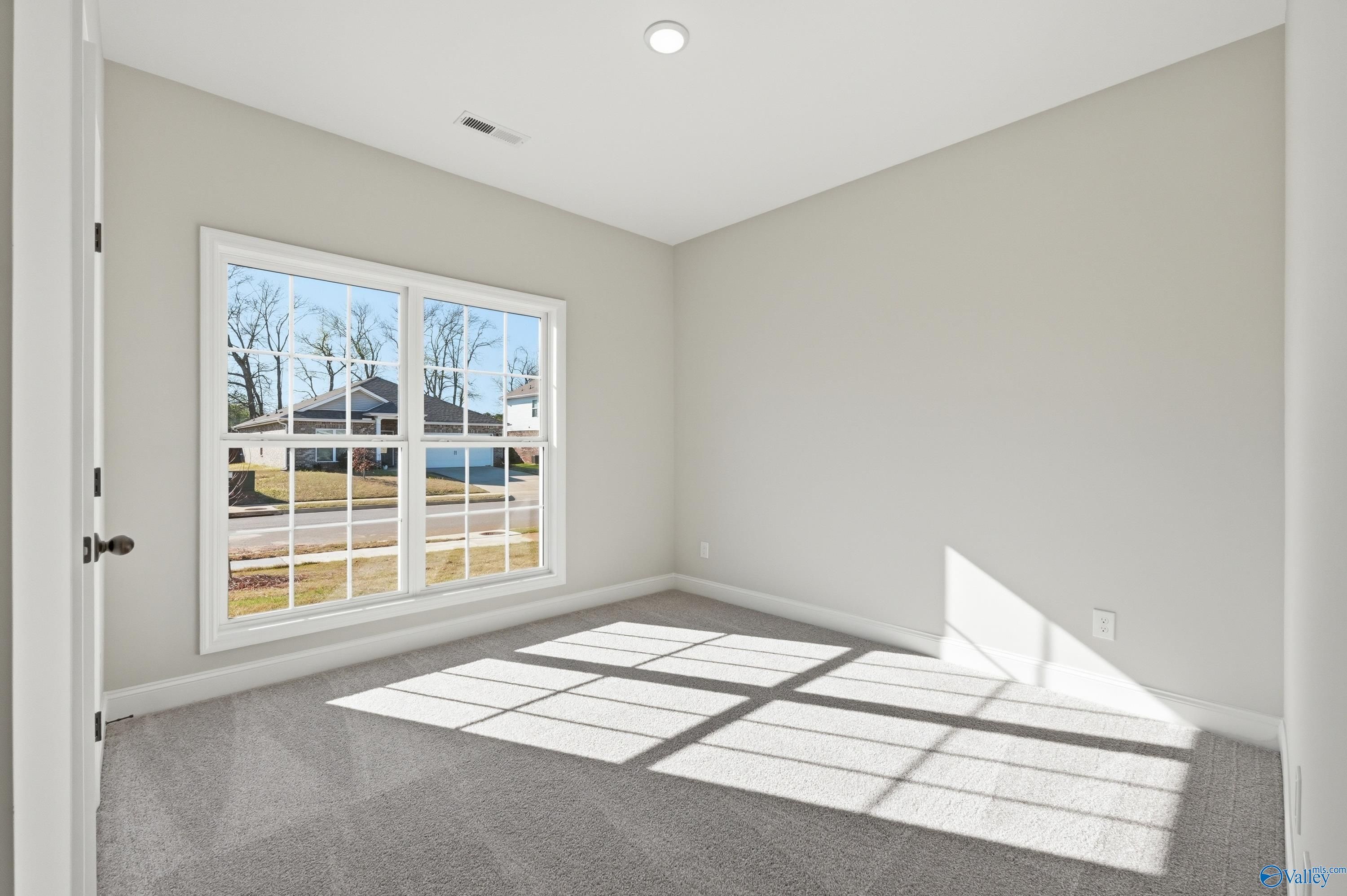 Bright bedroom with large window overlooking neighborhood trees, light gray walls, carpeted floor in Davidson Homes The Franklin C, New Market, Alabama