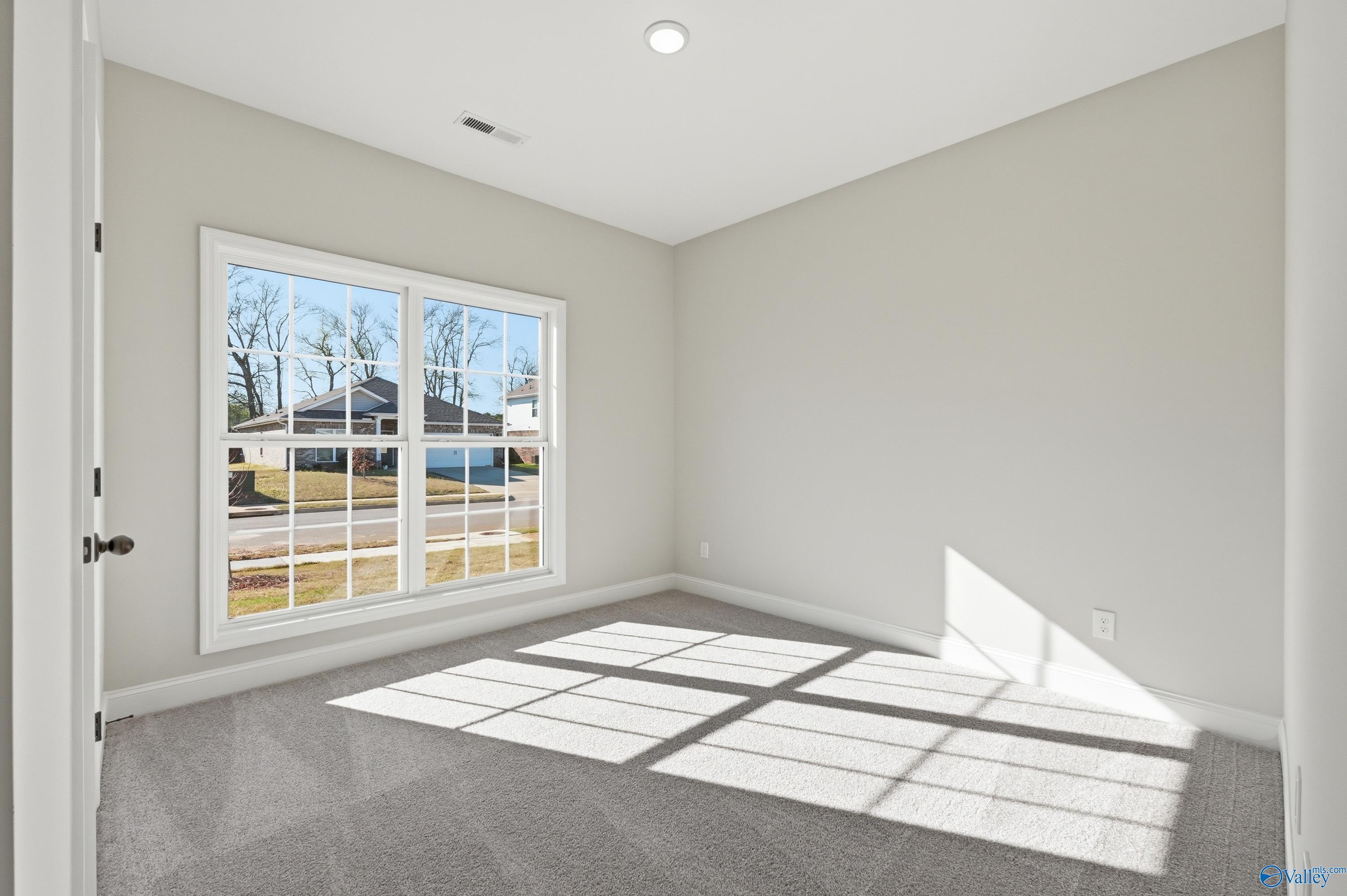 Bright bedroom with large window overlooking neighborhood trees, light gray walls, carpeted floor in Davidson Homes The Franklin C, New Market, Alabama