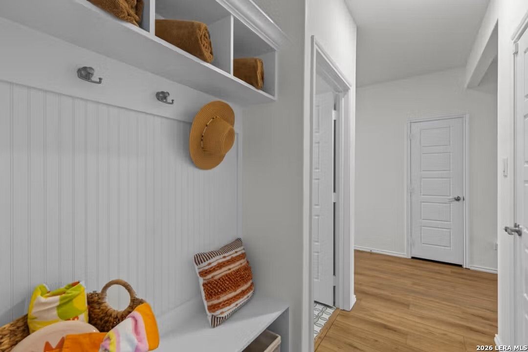 Organized mudroom with built-in white cabinet, towel shelves, hat hooks, and cushioned bench in Davidson Homes The Daphne H, Seguin, Texas