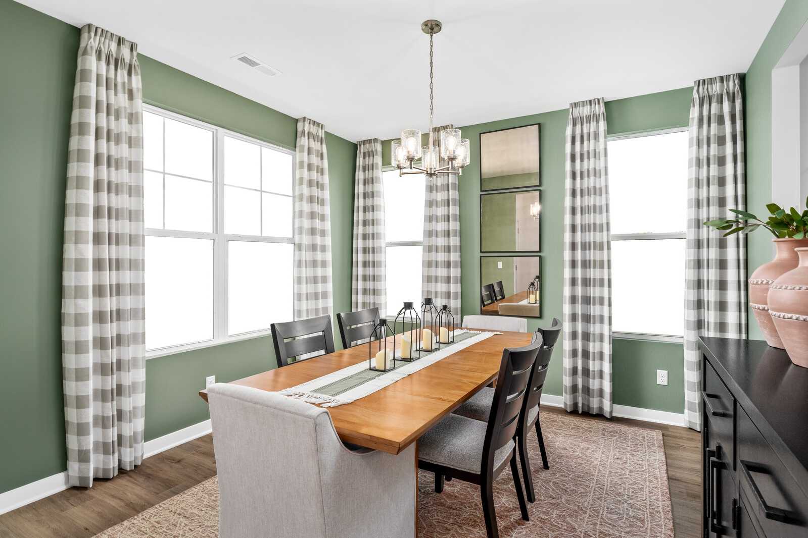 Spacious dining room at Calista Farms in White House TN with sage green walls, plaid curtains, wooden table, chandelier, and candle centerpiece
