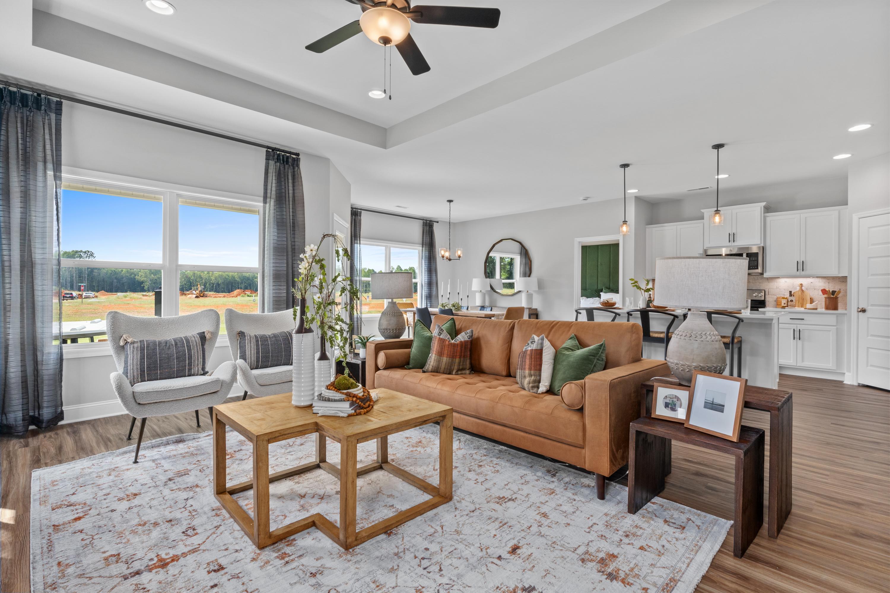 Open-concept living room at Wood Trail in Toney Alabama with tan leather sofa, wooden tables, kitchen island, and scenic field views