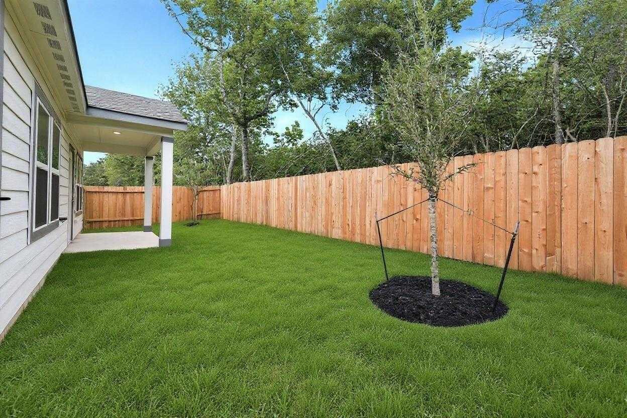 Covered patio and lush green backyard with young tree behind wooden fence in Davidson Homes The Frio G, Conroe, Texas