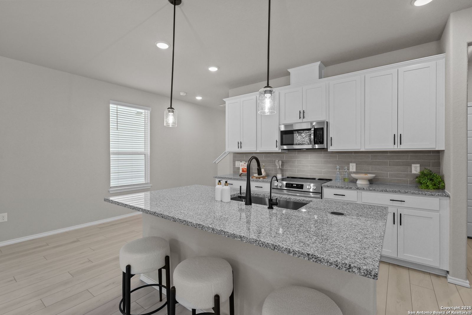 Modern kitchen featuring white shaker cabinets, granite island with bar stools, stainless appliances in Davidson Homes The Charlotte B, San Antonio