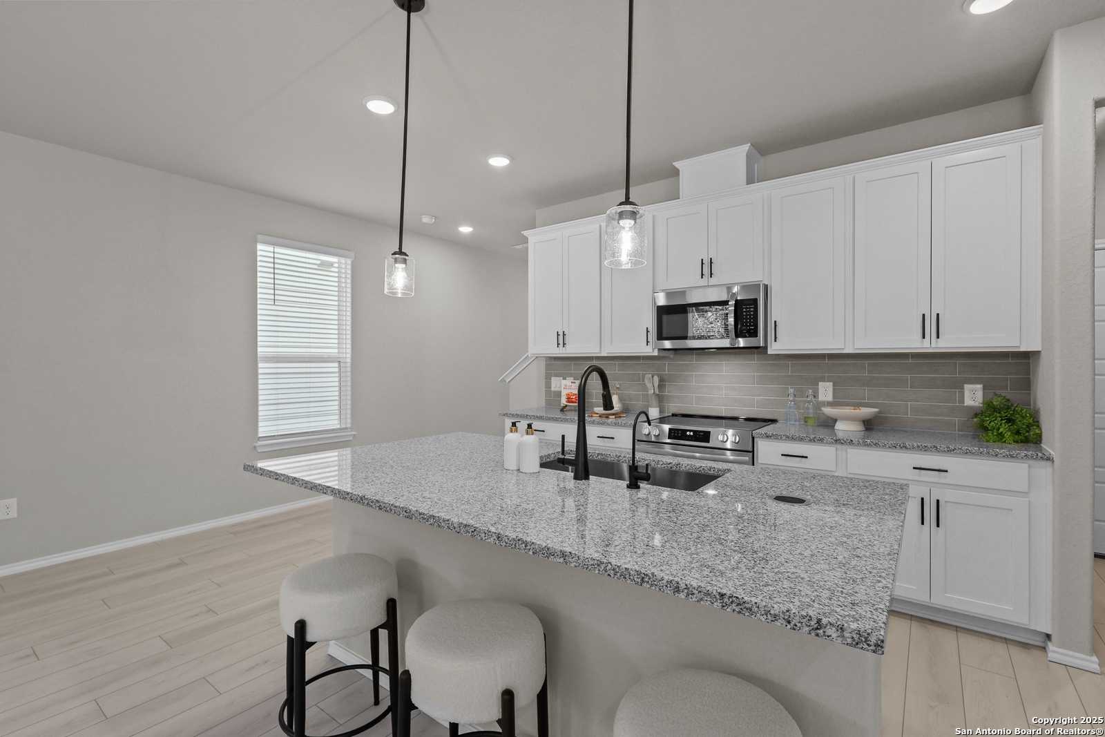 Modern kitchen featuring white shaker cabinets, granite island with bar stools, stainless appliances in Davidson Homes The Charlotte B, San Antonio