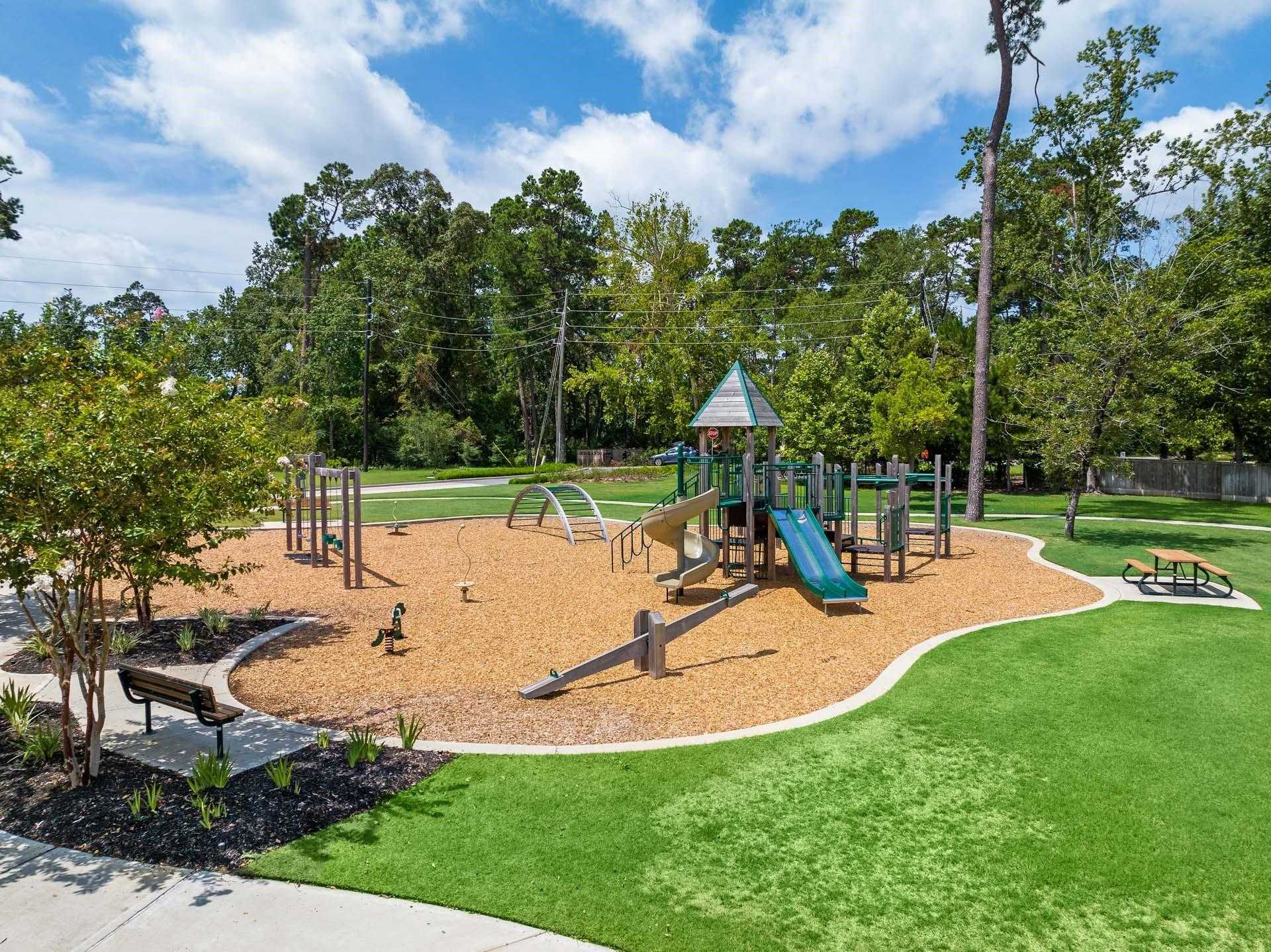 Vibrant playground with slides, climbers, swings, picnic table, and benches amid lush trees in Lakes at Black Oak, Magnolia, Texas