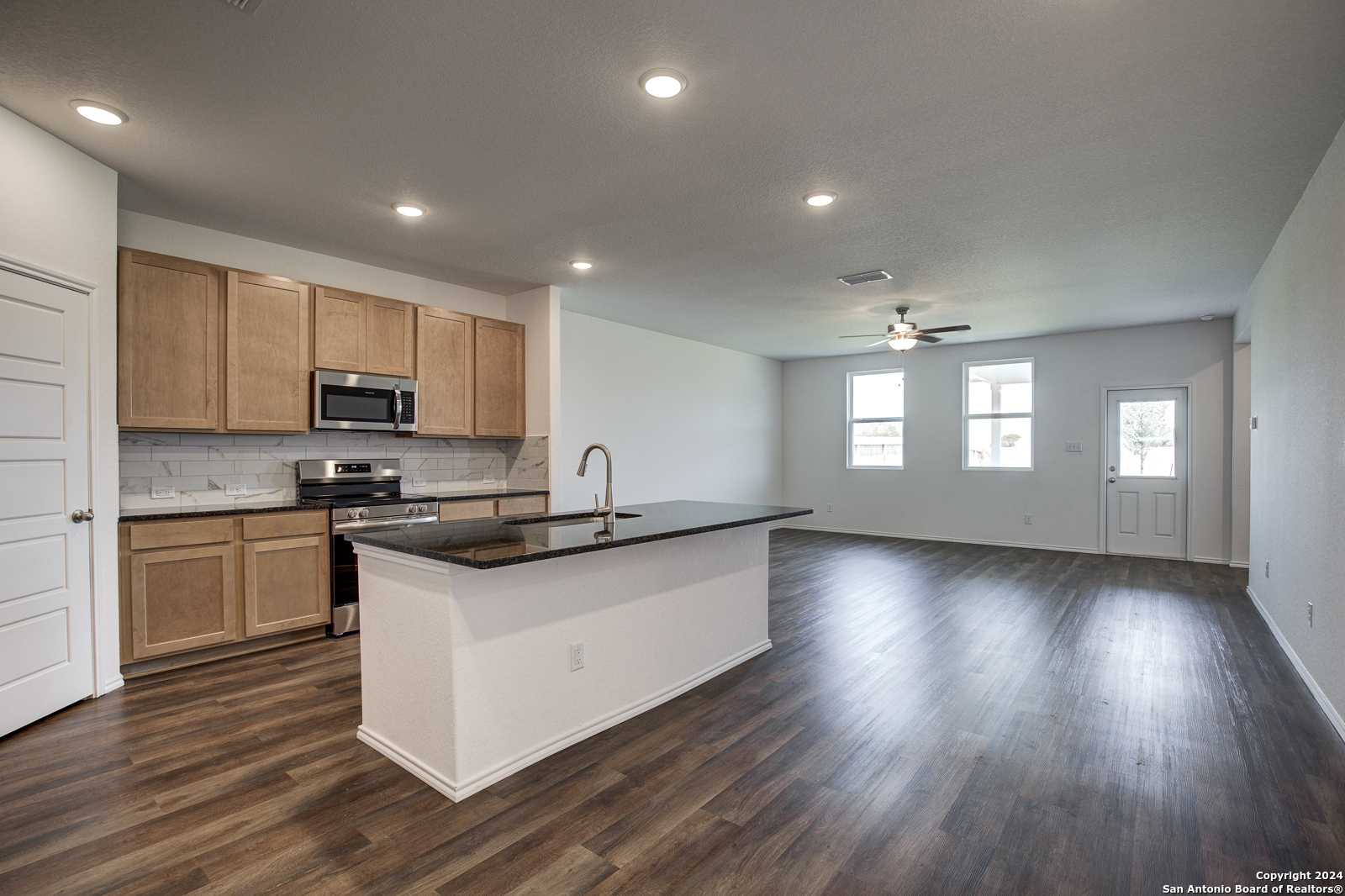 Modern open-concept kitchen with black granite island, stainless appliances, and hardwood floors in Davidson Homes The Douglas D, Seguin, Texas