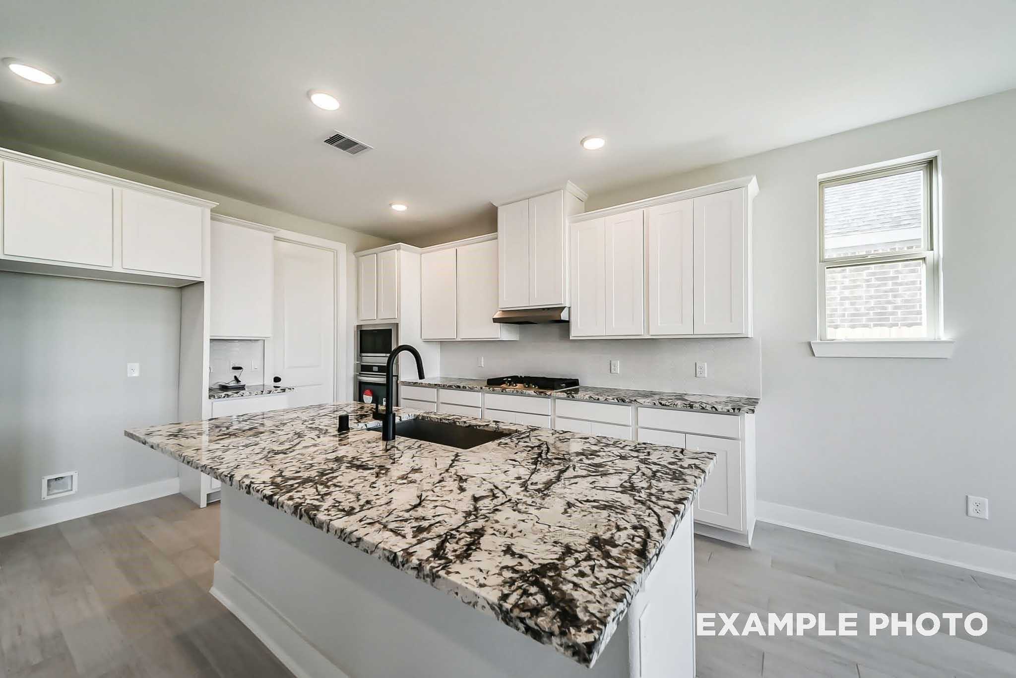 Contemporary kitchen with white cabinets, marbled granite island, black faucet, stainless appliances in Davidson Homes The Philip C, Rosharon, Texas
