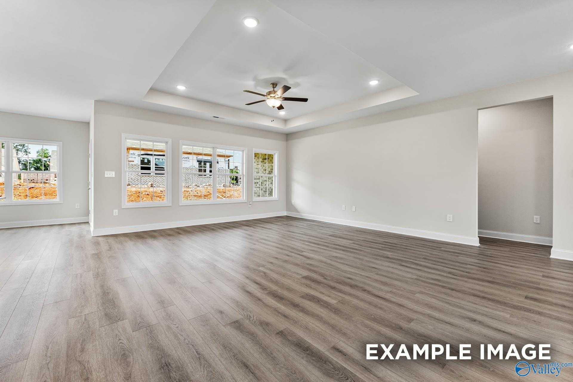 Spacious open living room with hardwood floors, ceiling fan, and large windows in The Finleigh by Davidson Homes, Meridianville, AL