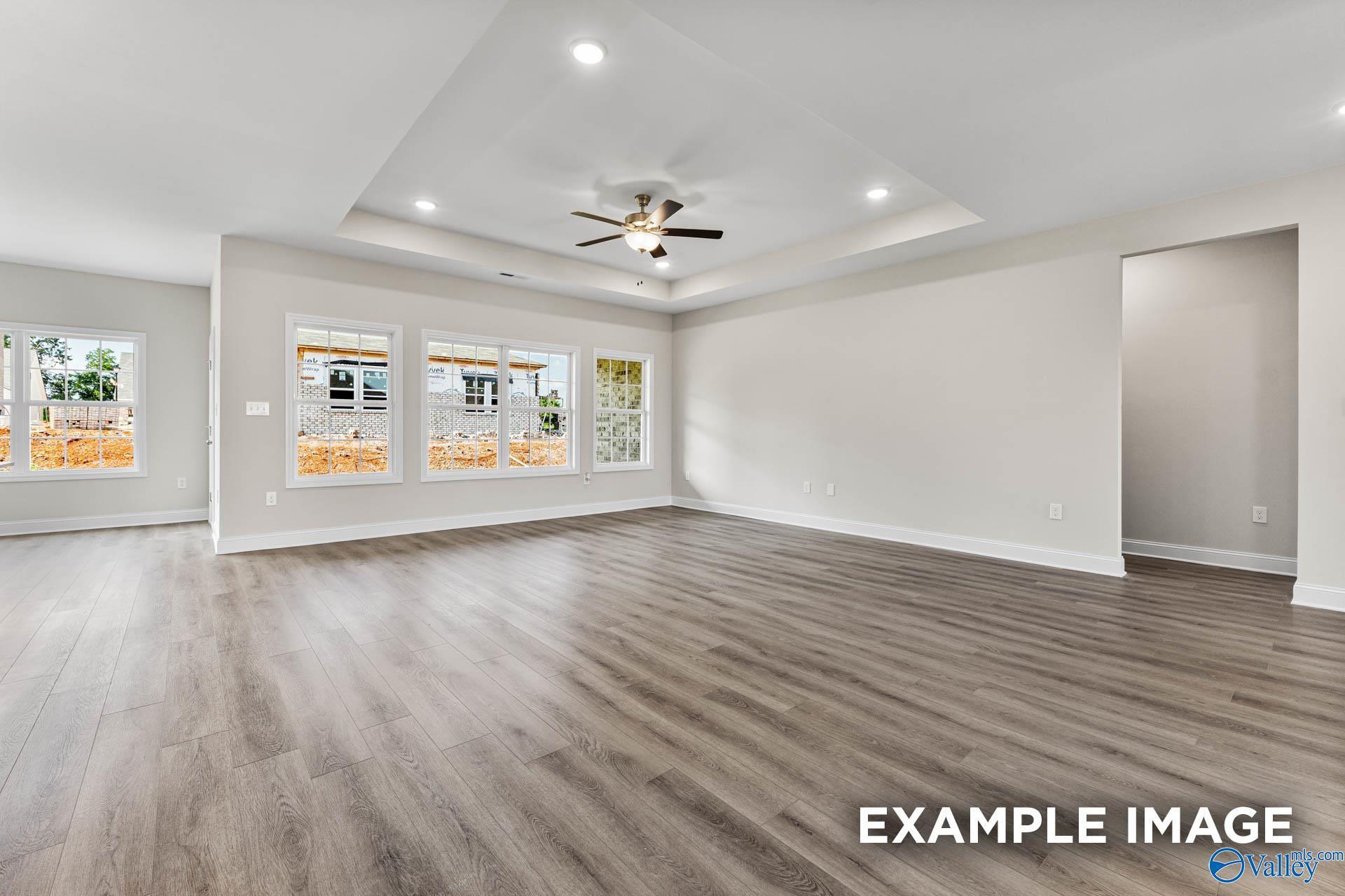 Spacious open living room with hardwood floors, ceiling fan, and large windows in Davidson Homes The Finleigh, Meridianville, Alabama