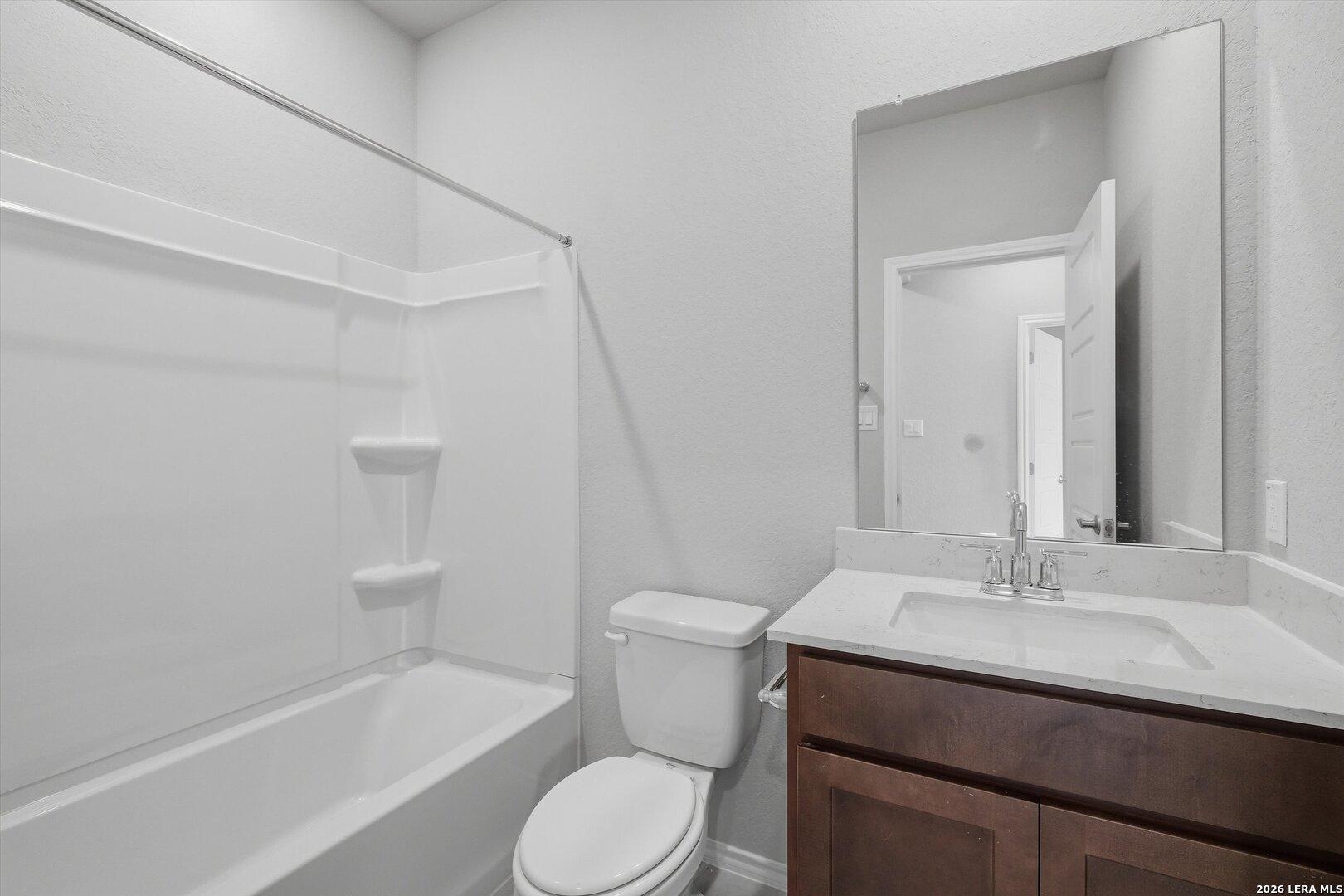 Modern guest bathroom featuring white tub-shower combo, quartz countertop vanity, wood cabinets, and large mirror in Davidson Homes The Frio B, San Antonio, Texas