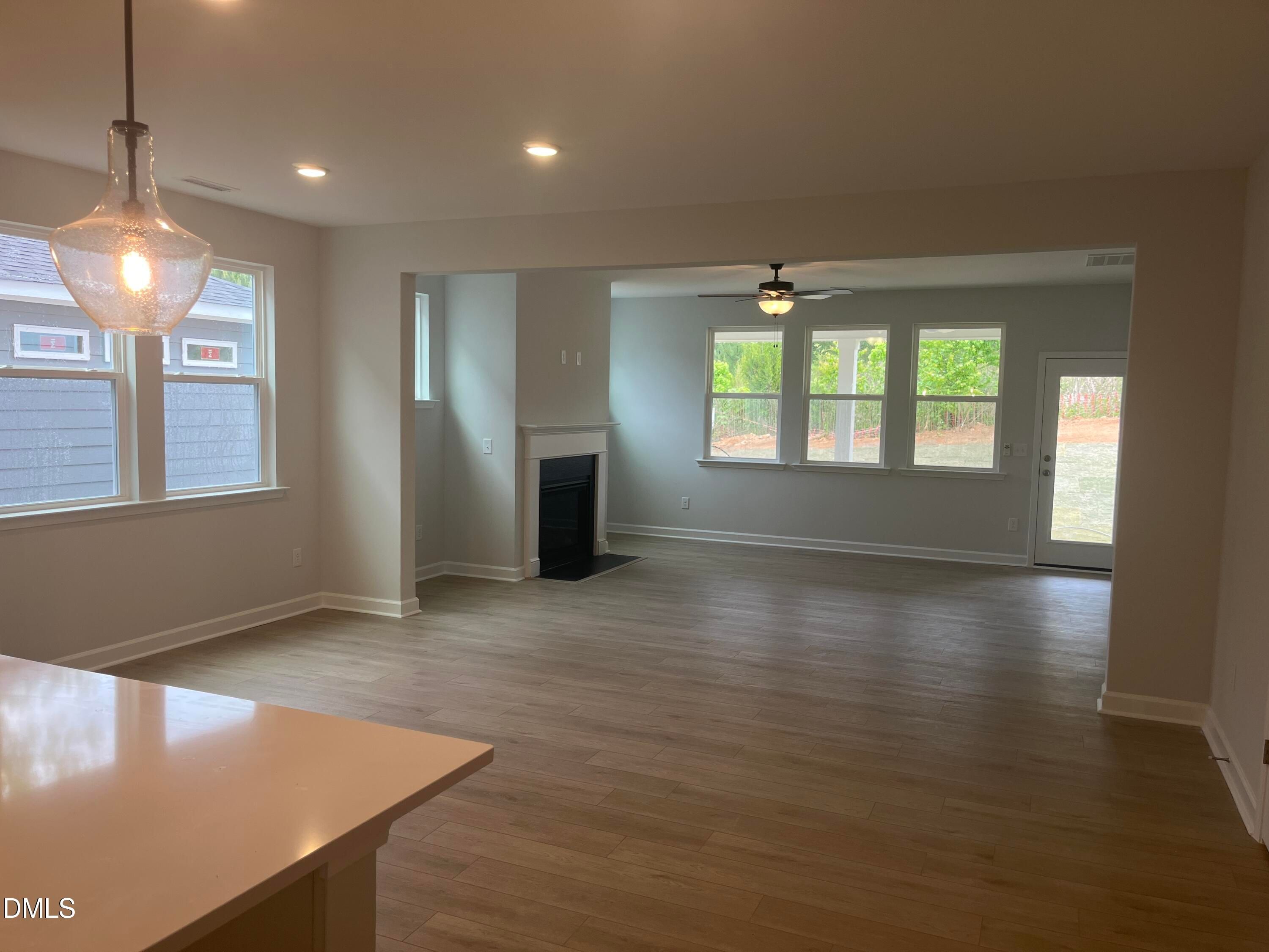 Open living area with white kitchen island, gas fireplace, hardwood floors, and backyard views in The Birch II E, Wake Forest, NC
