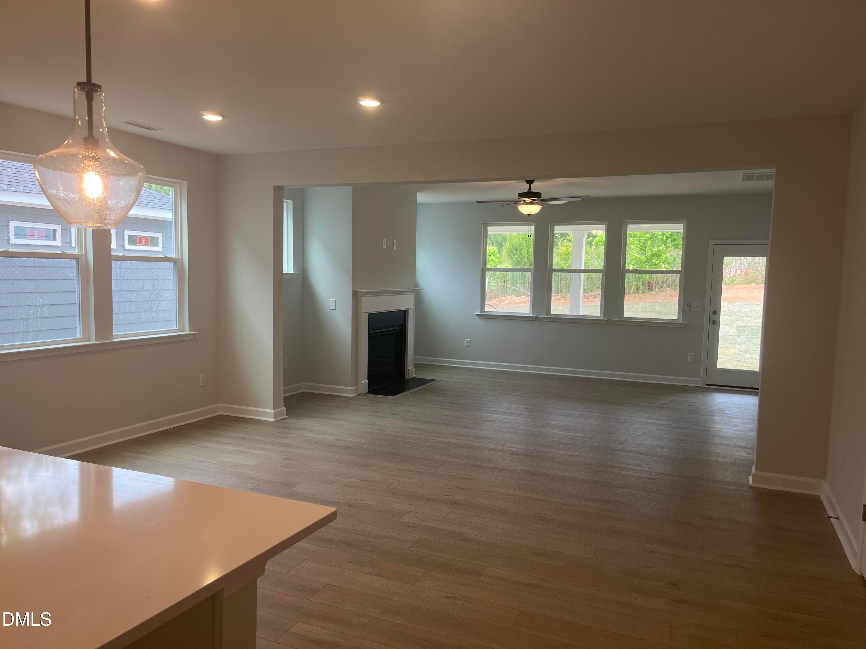 Open living area with white kitchen island, gas fireplace, hardwood floors, and backyard views in The Birch II E, Wake Forest, NC