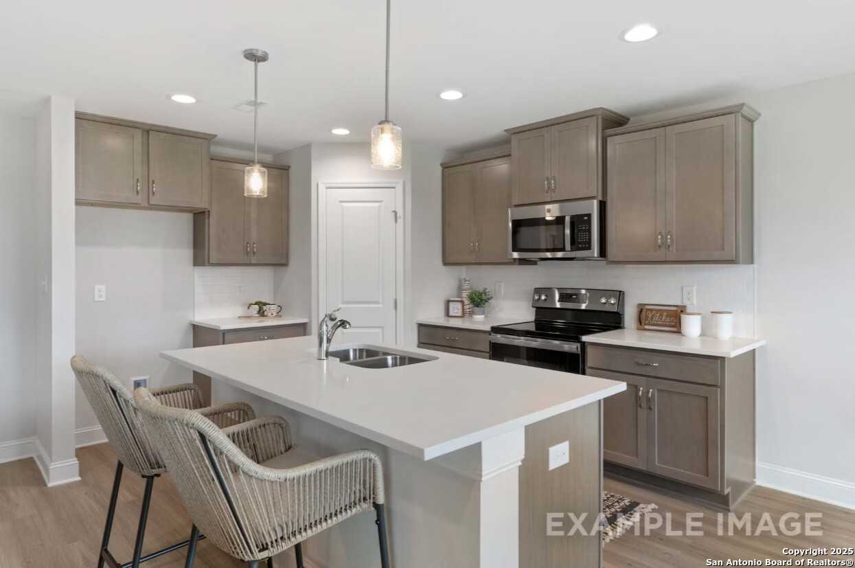 Modern kitchen with white quartz island, stainless appliances, pendant lights in Davidson Homes The Asheville K, Bricewood, San Antonio