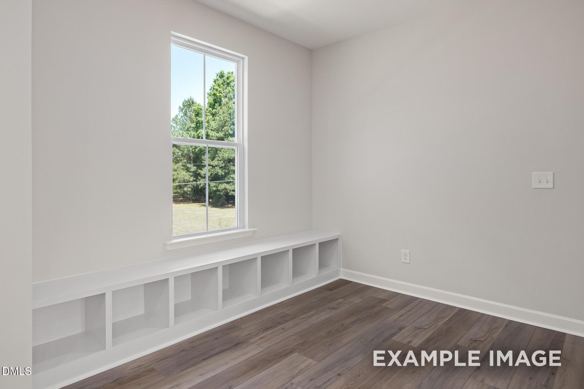 Bright bedroom with built-in storage bench and wood-look flooring in The Mitchell floor plan at Camden Park, Knightdale.