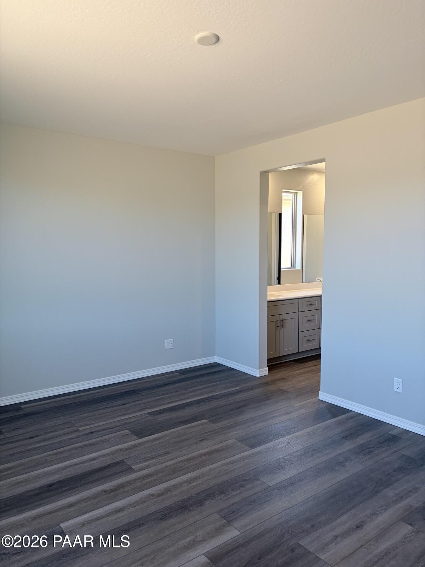 Spacious bedroom with wood-look flooring leading to a bathroom vanity in The Frontier A at Pronghorn Ranch, Prescott Valley.