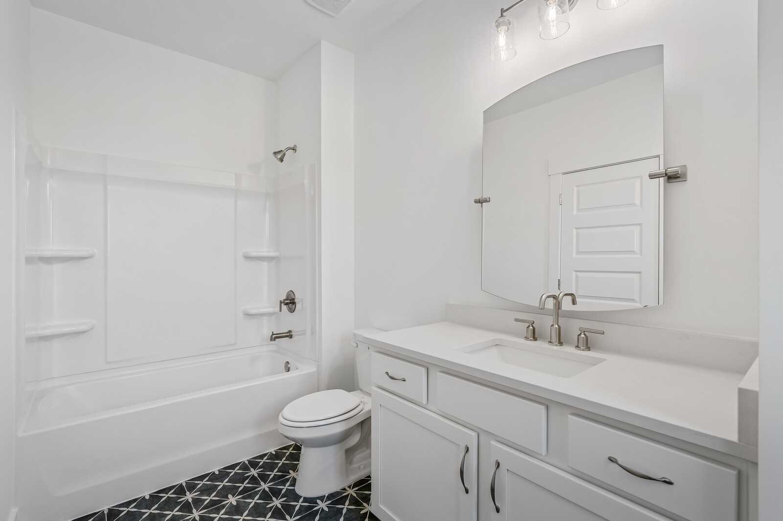 Bright white guest bathroom with double vanity, deep tub, and patterned tile floor in Davidson Homes The Hawkins, Murfreesboro, TN