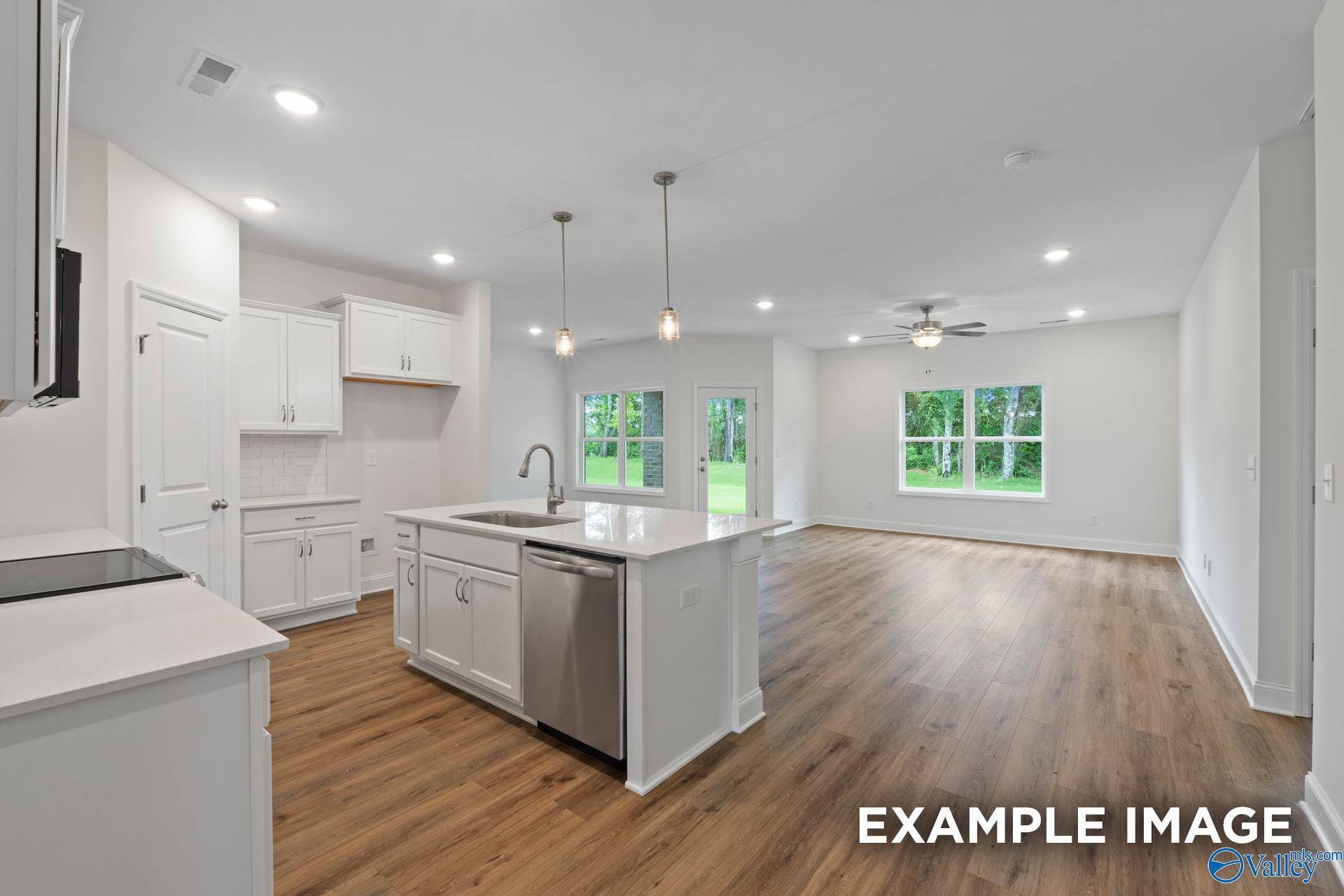 Bright open-concept kitchen with white cabinets, island sink, and backyard views in The Daphne E 4-bedroom home, Harvest, AL