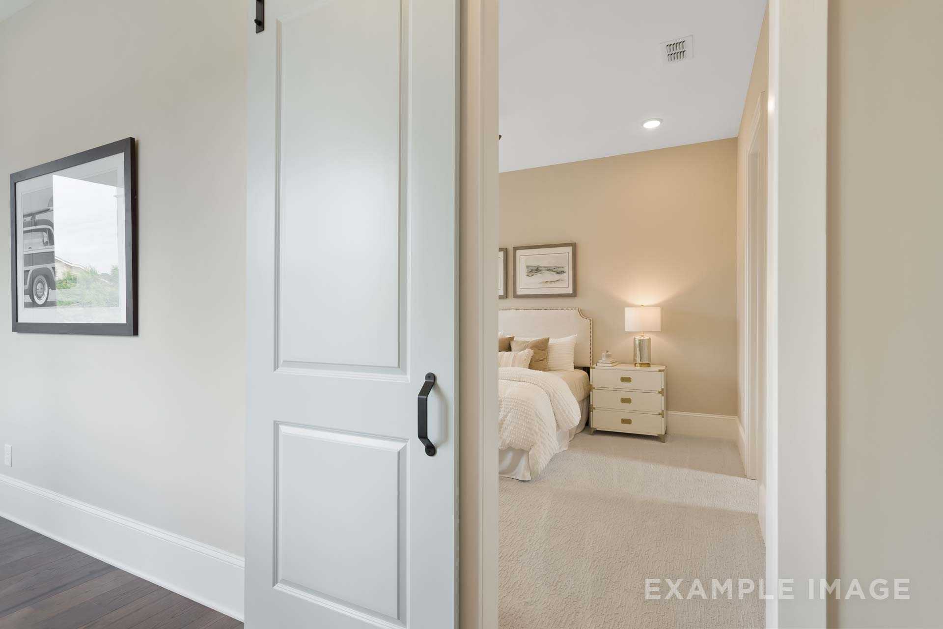Spacious master bedroom in The Seaside home design featuring king bed, nightstands, lamps, and open white doorway