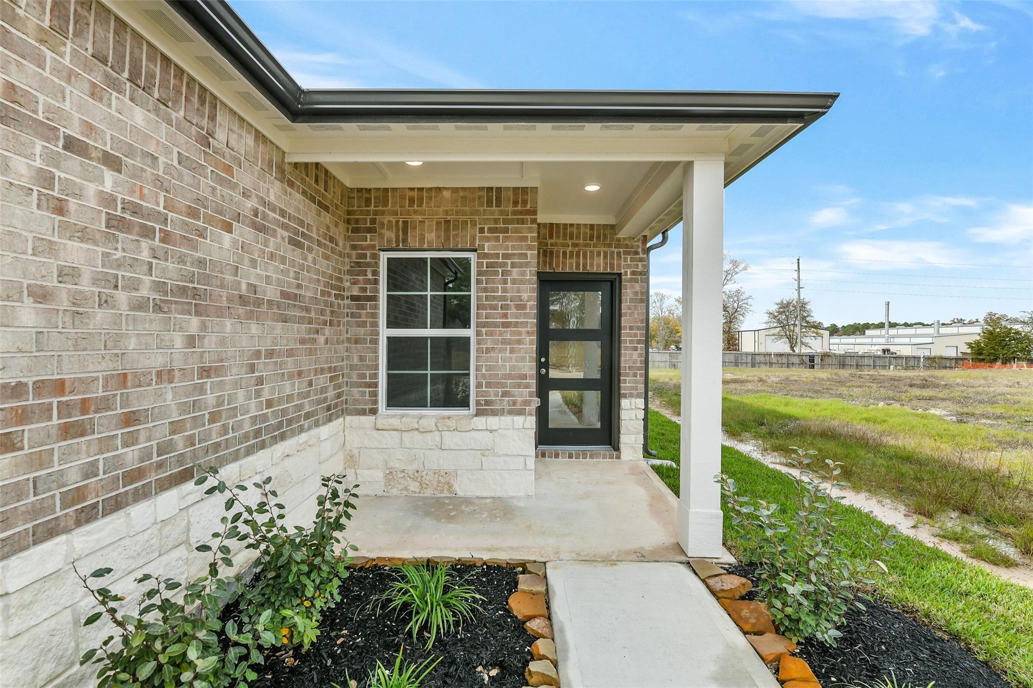 Modern brick facade with covered porch, black glass entry door, stone accents, and landscaped shrubs in Davidson Homes The Colorado G, Magnolia TX