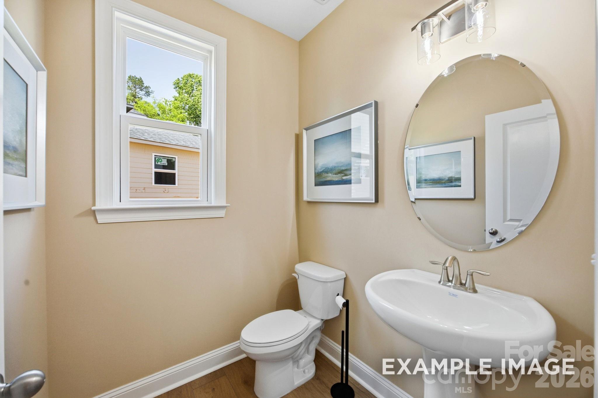 Modern half-bath with pedestal sink, oval mirror, and neutral walls in a Davidson Homes Hickory B II floor plan home.