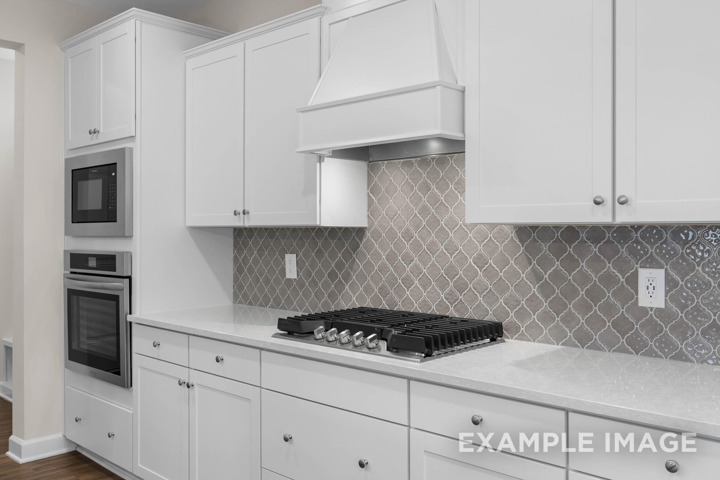Spacious kitchen in The Gavin B featuring white shaker cabinets, double oven, gas cooktop, and gray patterned backsplash