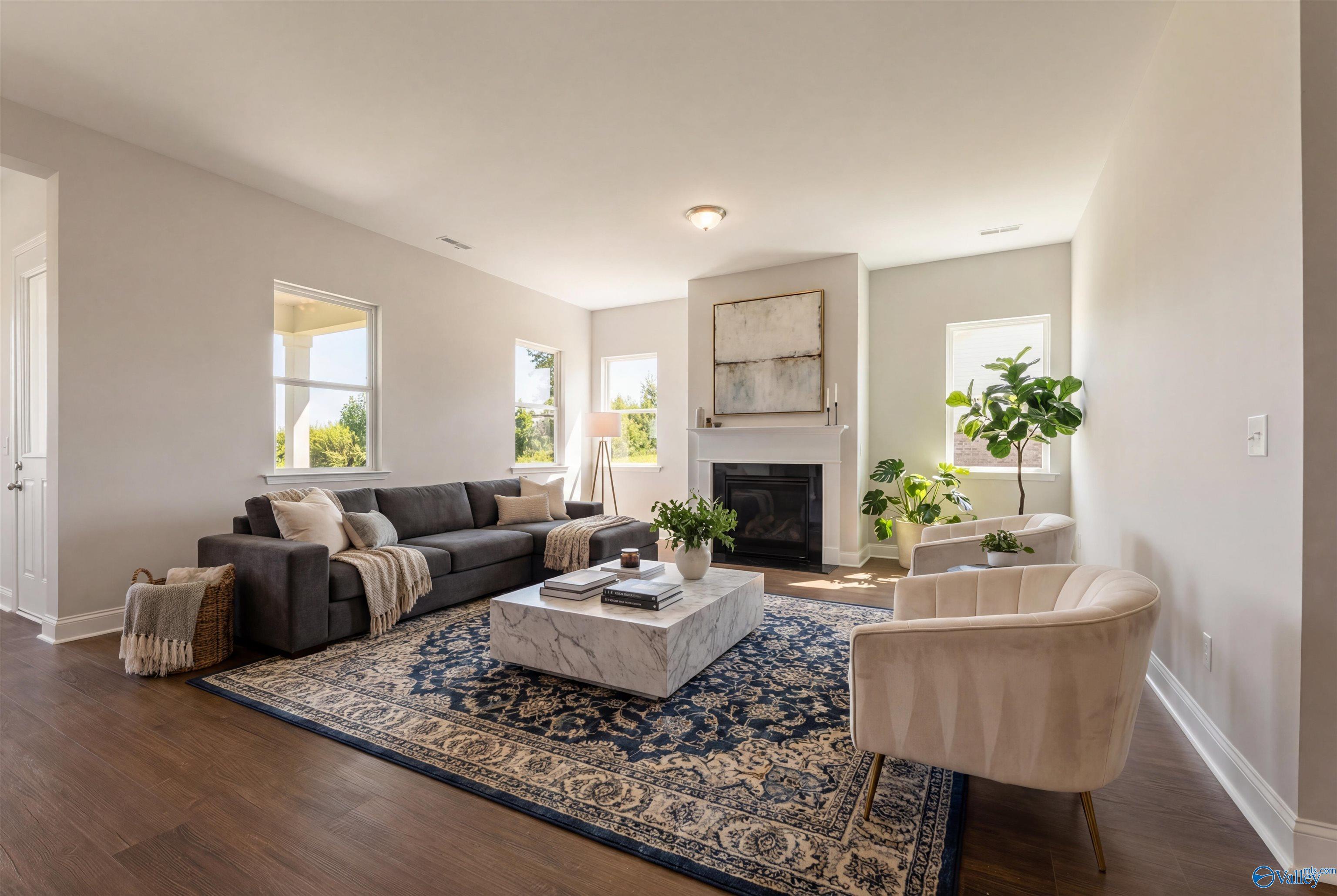 Cozy living room with gray L-shaped sofa, white marble coffee table, blue rug, and gas fireplace in Davidson Homes The Arcadia B, Huntsville, AL
