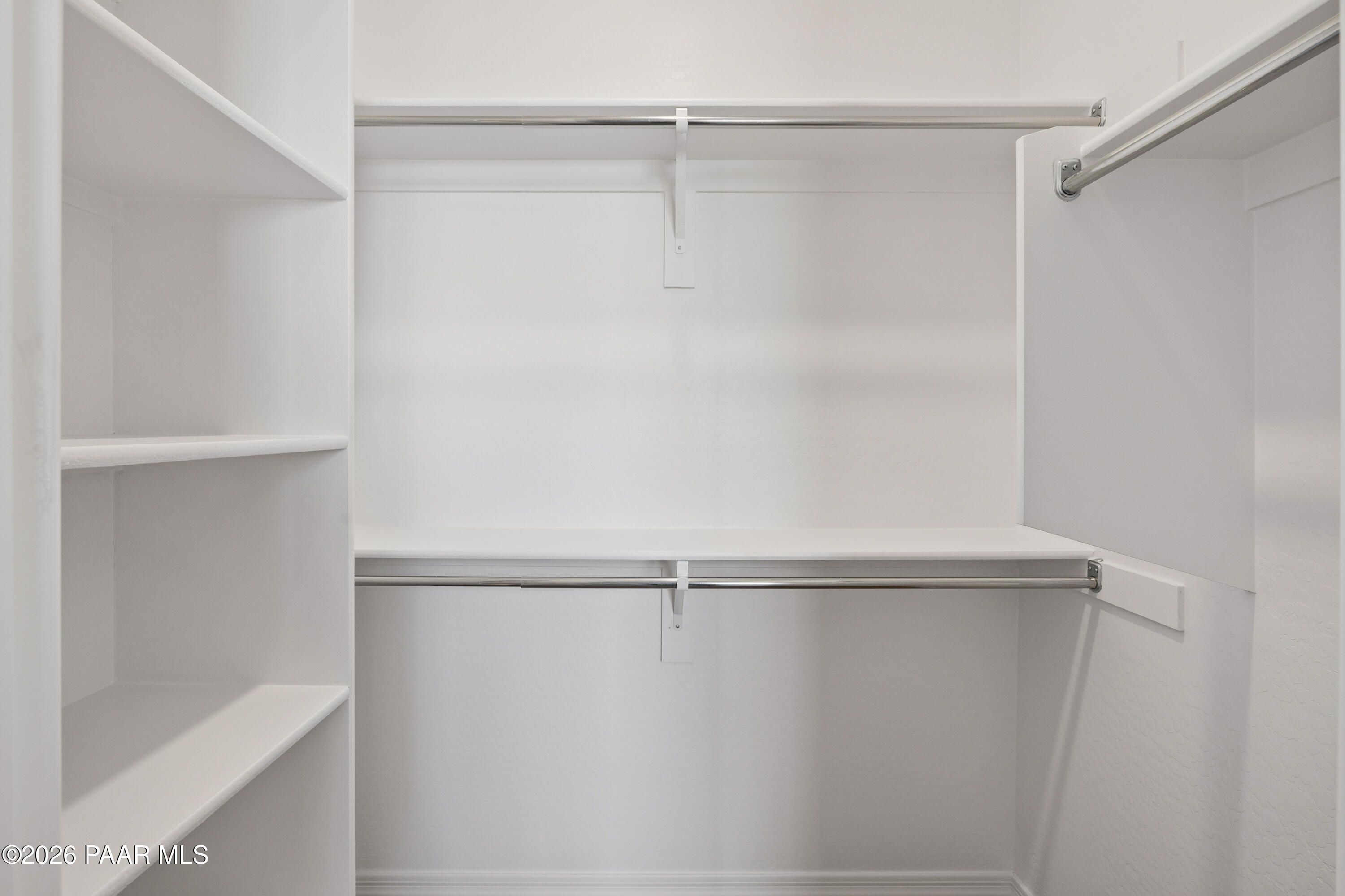 Spacious walk-in closet with white shelves and hanging rods in Davidson Homes The Harmony A, Prescott Valley, Arizona
