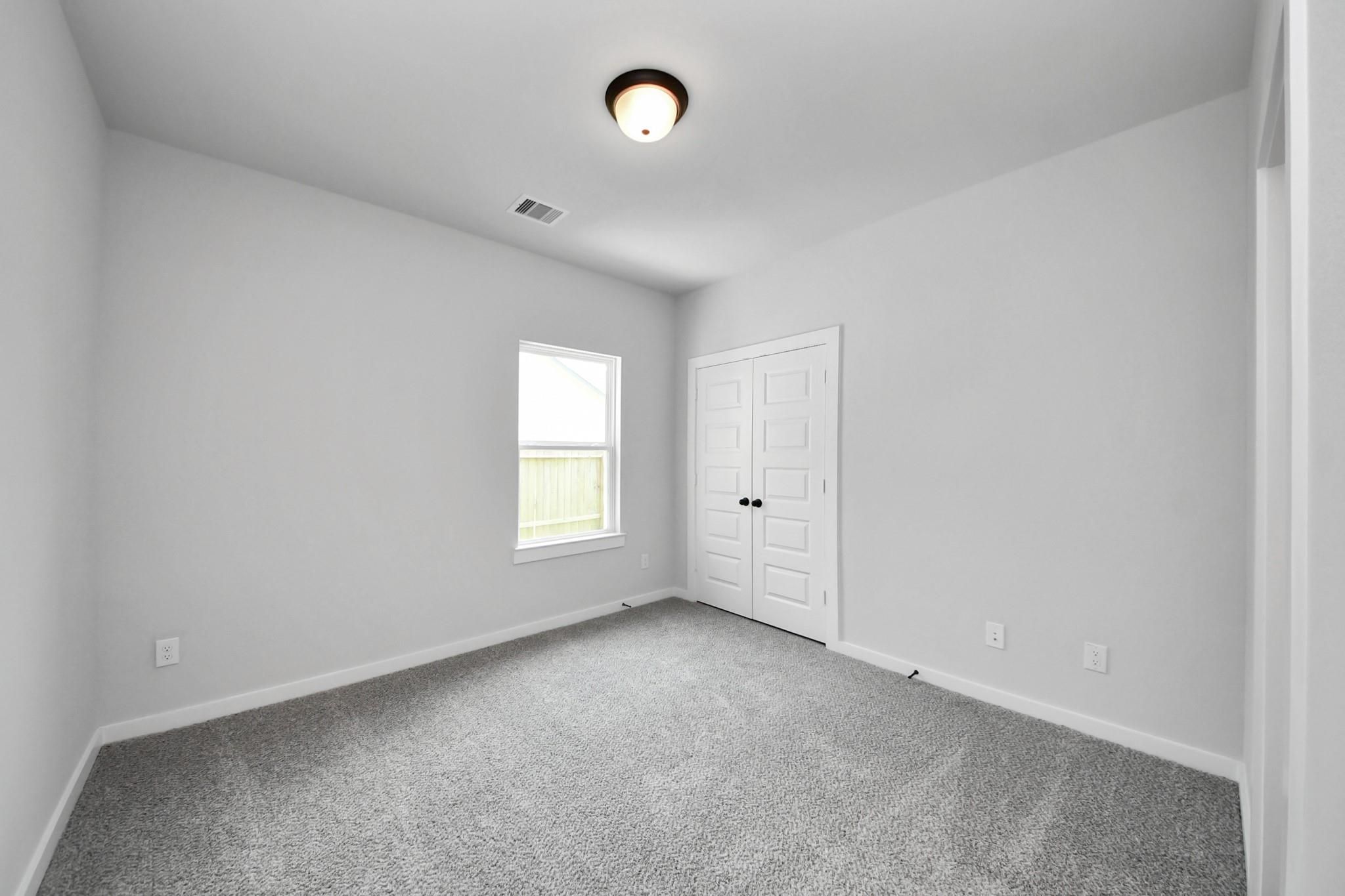 Bright, carpeted bedroom with closet in The Everett C floor plan at River Ranch Meadows in Dayton, Texas.