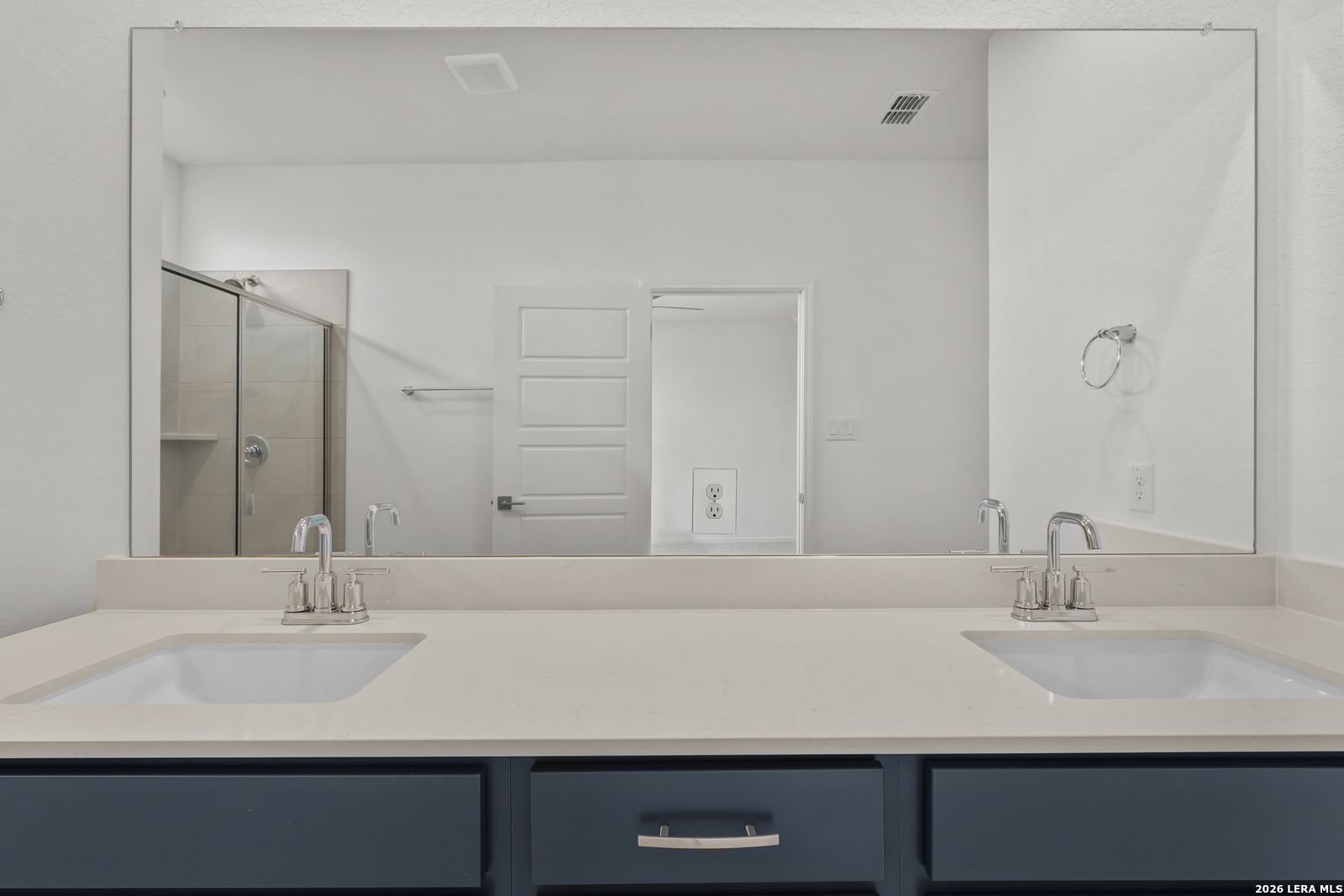 Modern master bathroom double vanity with quartz countertop, navy cabinets, and glass shower in Davidson Homes The Glenwood E, Elmendorf Texas