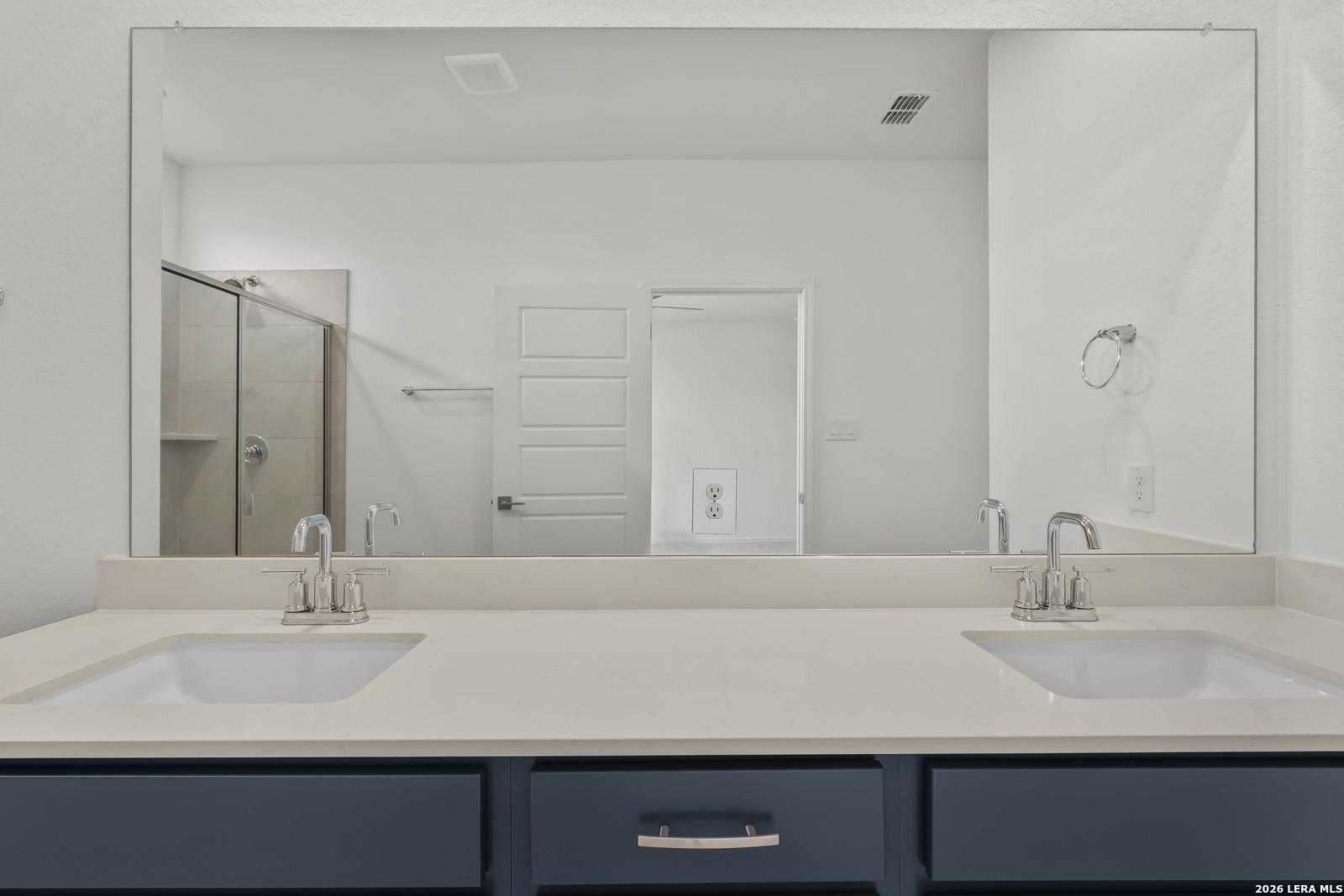 Modern master bathroom double vanity with quartz countertop, navy cabinets, and glass shower in Davidson Homes The Glenwood E, Elmendorf Texas