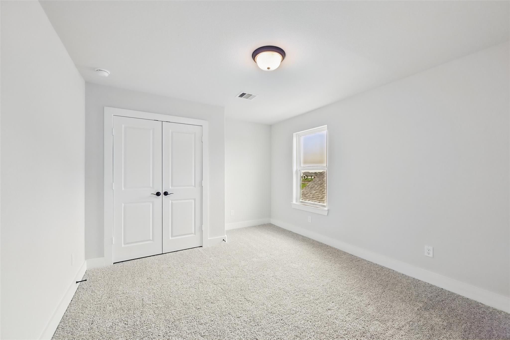 Bright secondary bedroom featuring white walls, gray carpet, double closet doors, and window in Davidson Homes The Victoria C, Lago Mar, Texas City