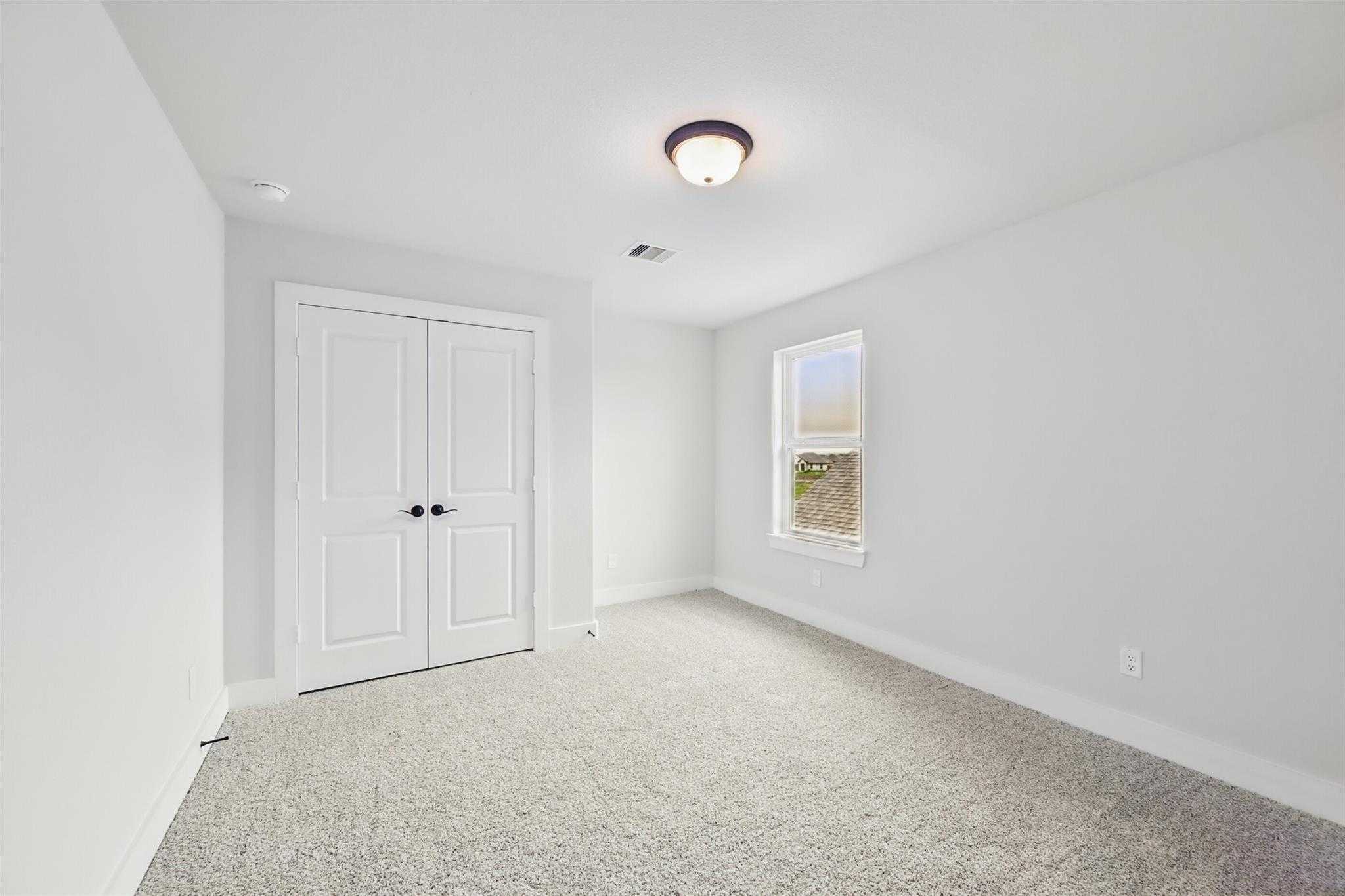 Bright secondary bedroom with light gray walls, white double doors, carpeted floor, and window in Davidson Homes Victoria C, Lago Mar, Texas City
