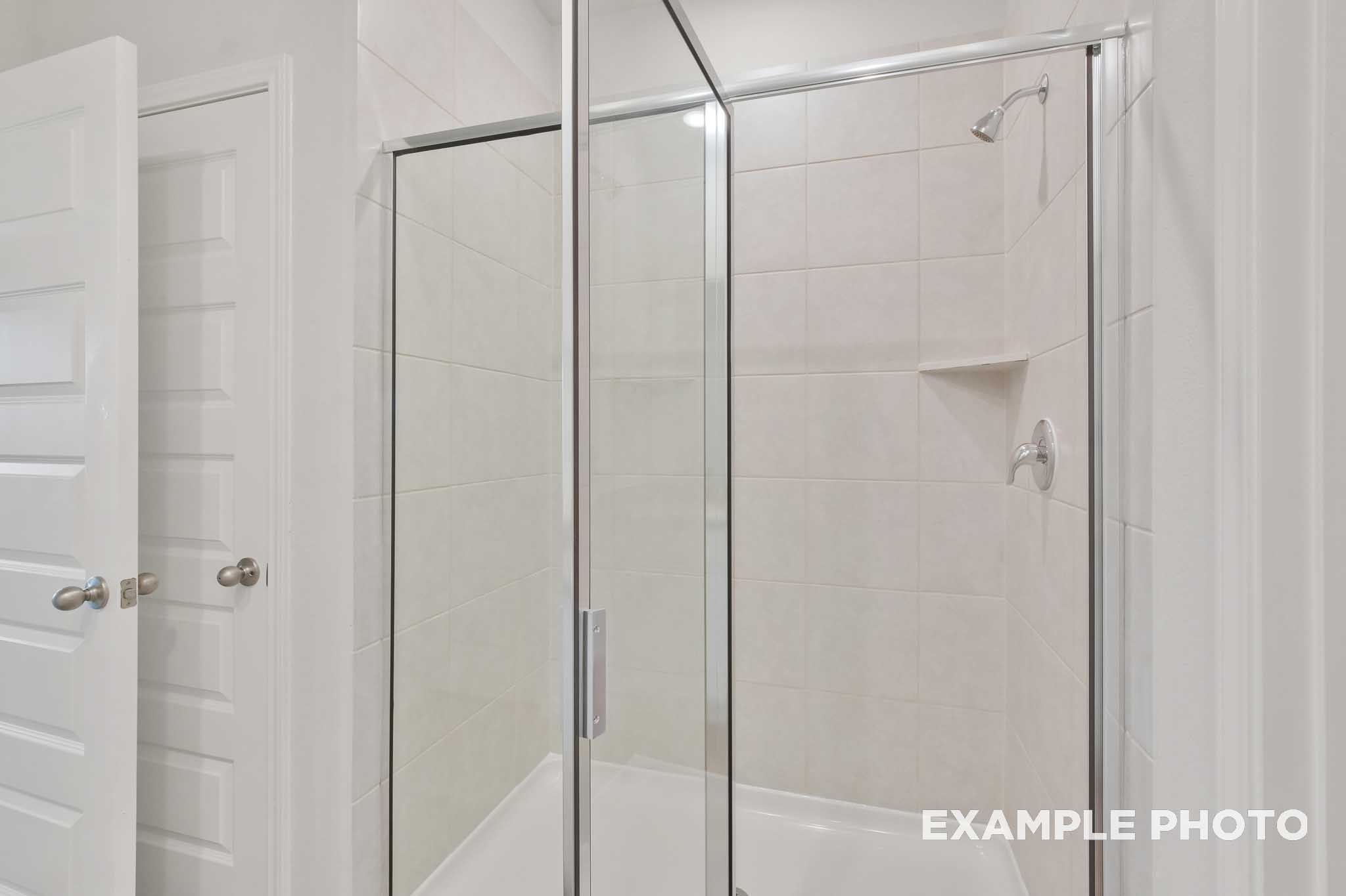 Glass-enclosed tile shower with brushed nickel fixtures in The Brazos master bathroom by Davidson Homes, Beasley, Texas